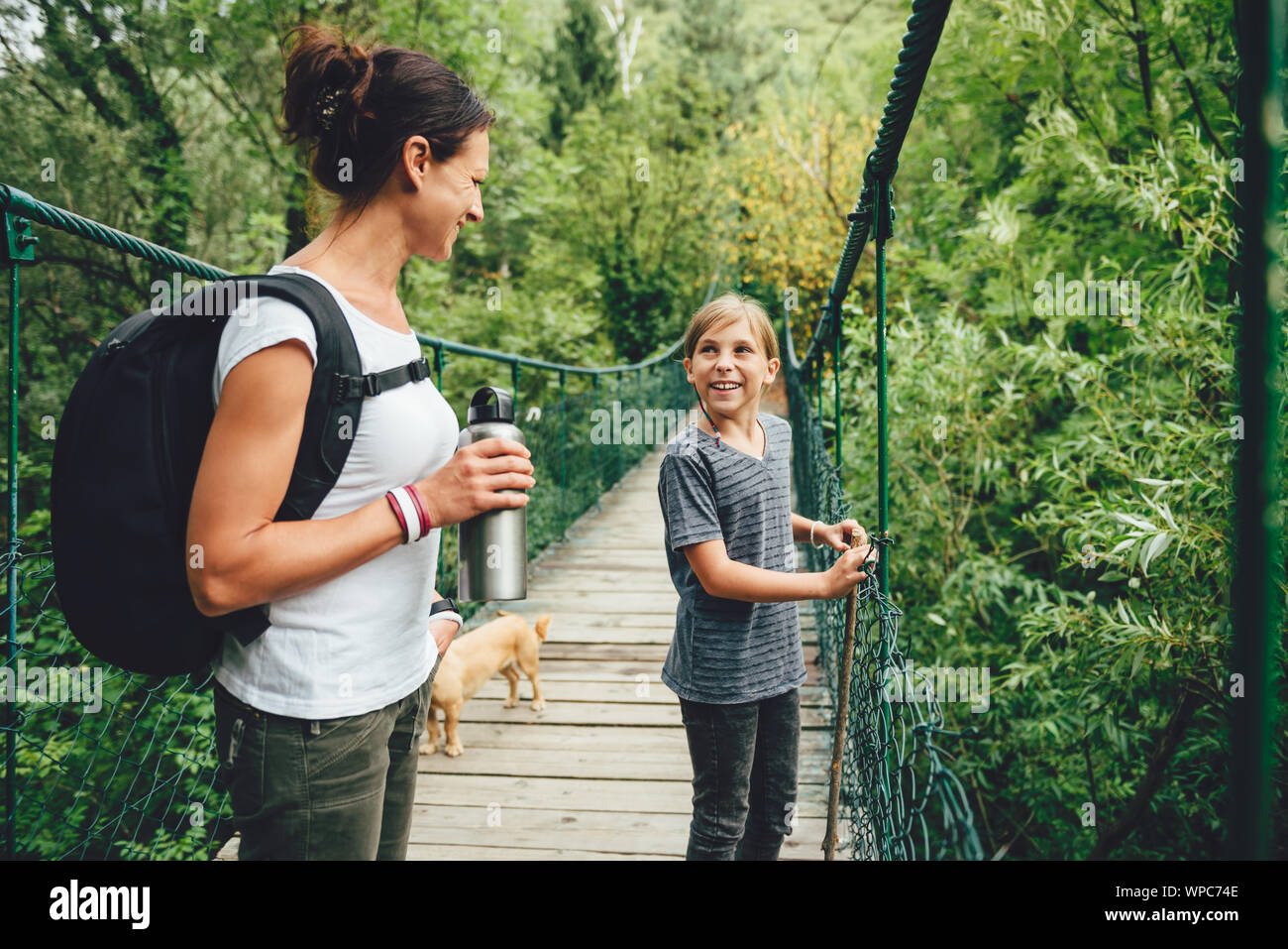 Mère et fille debout sur le pont suspendu en bois avec petit chien jaune et de parler Banque D'Images Mère et fille debout sur le pont suspendu en bois avec petit chien jaune et de parler Banque D'Images