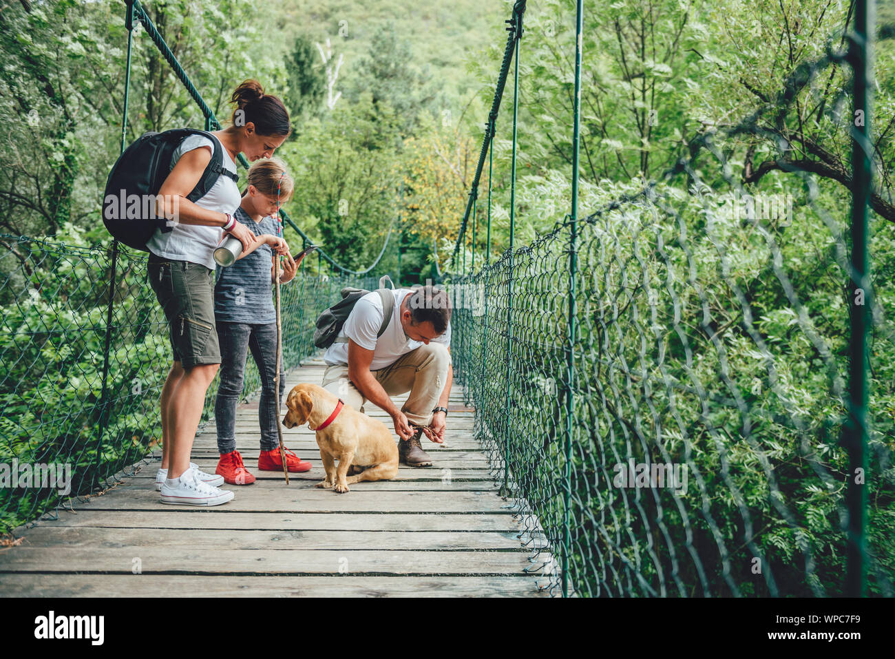 Famille avec chien debout sur un pont suspendu en bois et à l'aide de smart phone pour naviguer Banque D'Images