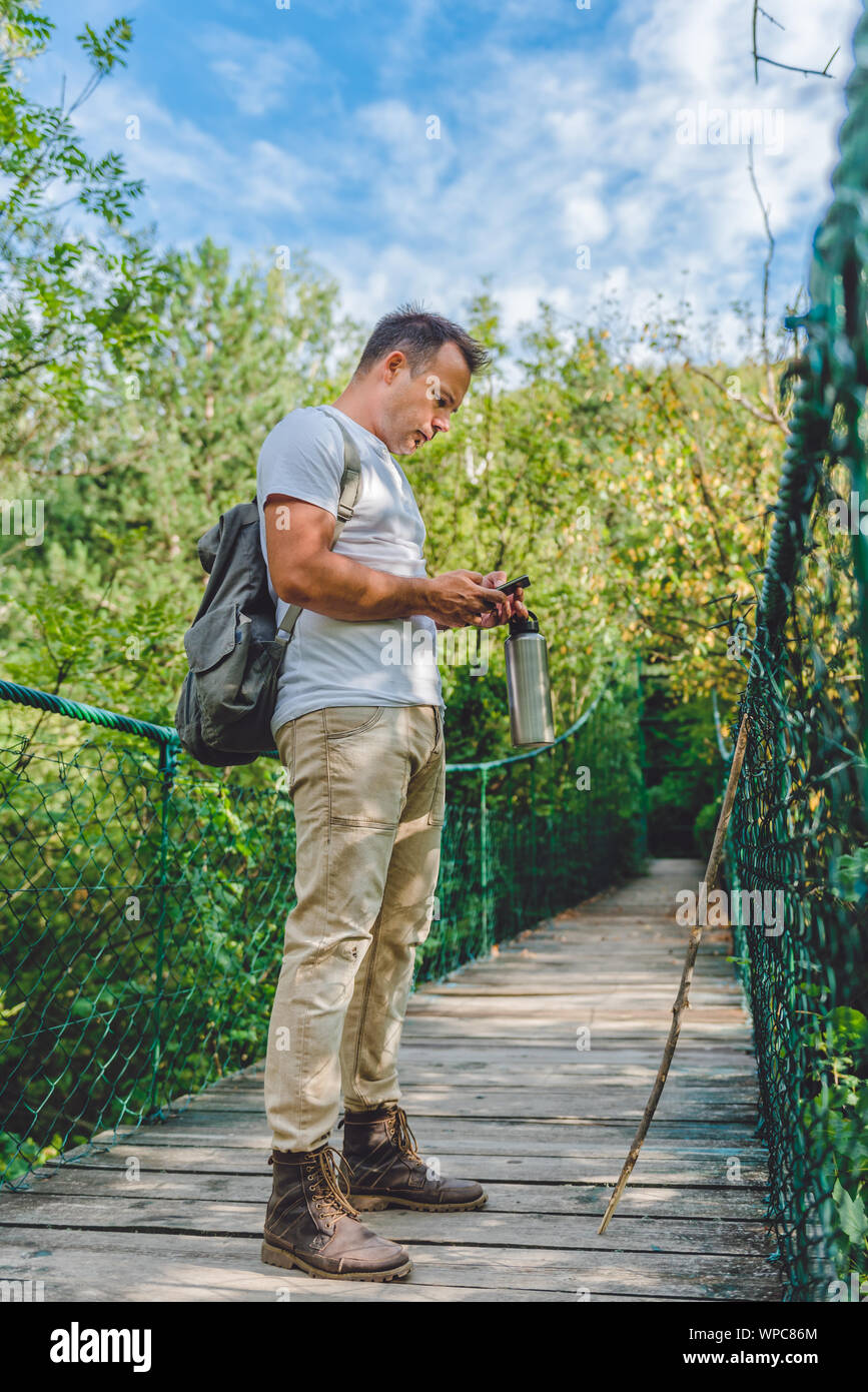 Randonneur debout sur le pont suspendu en bois dans la forêt et l'utilisation de smart phone pour naviguer Banque D'Images