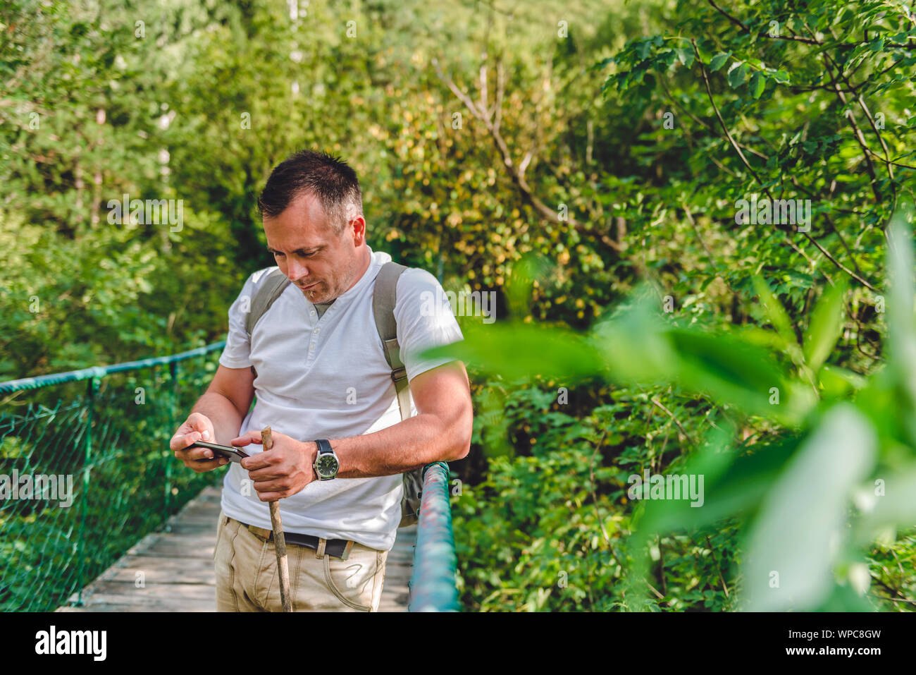 Randonneur debout sur le pont suspendu en bois dans la forêt et l'utilisation de smart phone Banque D'Images