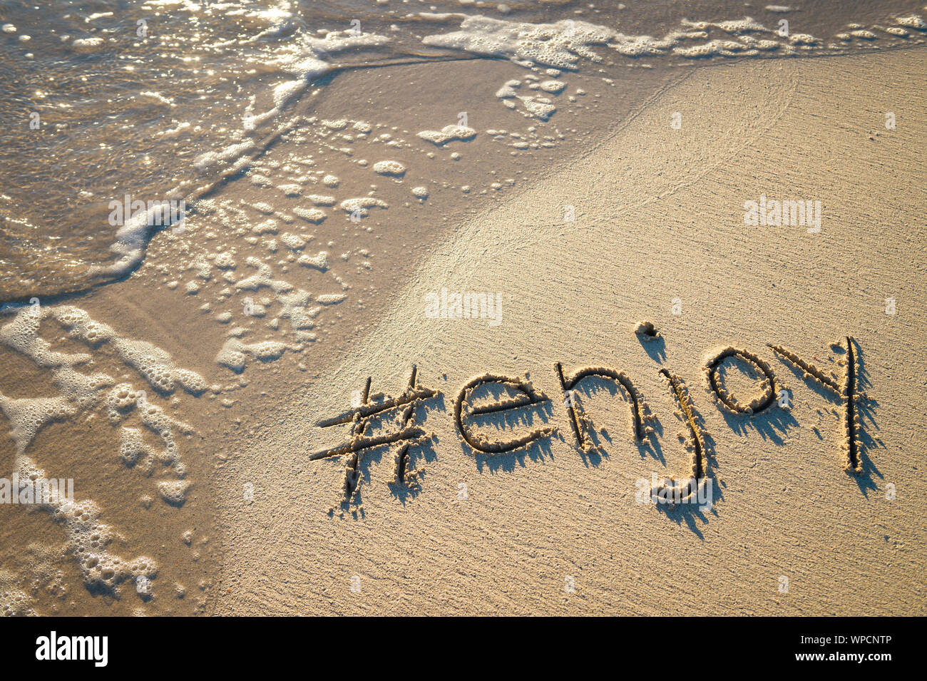 Message de voyage modernes pour la plage 'profiter' écrit avec un social media-friendly hashtag dans le sable avec l'onde lisse Banque D'Images