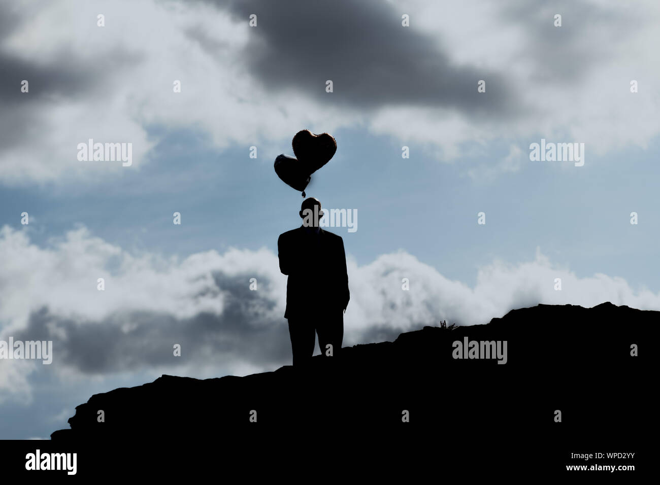 Un homme de coeur ballon. Des symboles. Un homme avec deux cœurs balloon se dresse sur une colline en face de ciel bleu avec des nuages Banque D'Images
