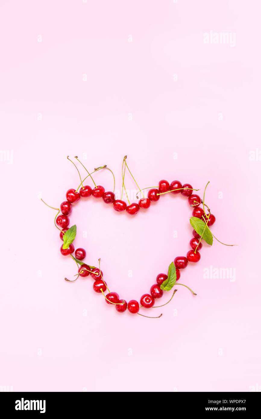 Photo verticale pour blog ou histoire. Petits fruits cerise rouge en forme de coeur sur fond rose. Mise à plat. Concept alimentaire. Banque D'Images