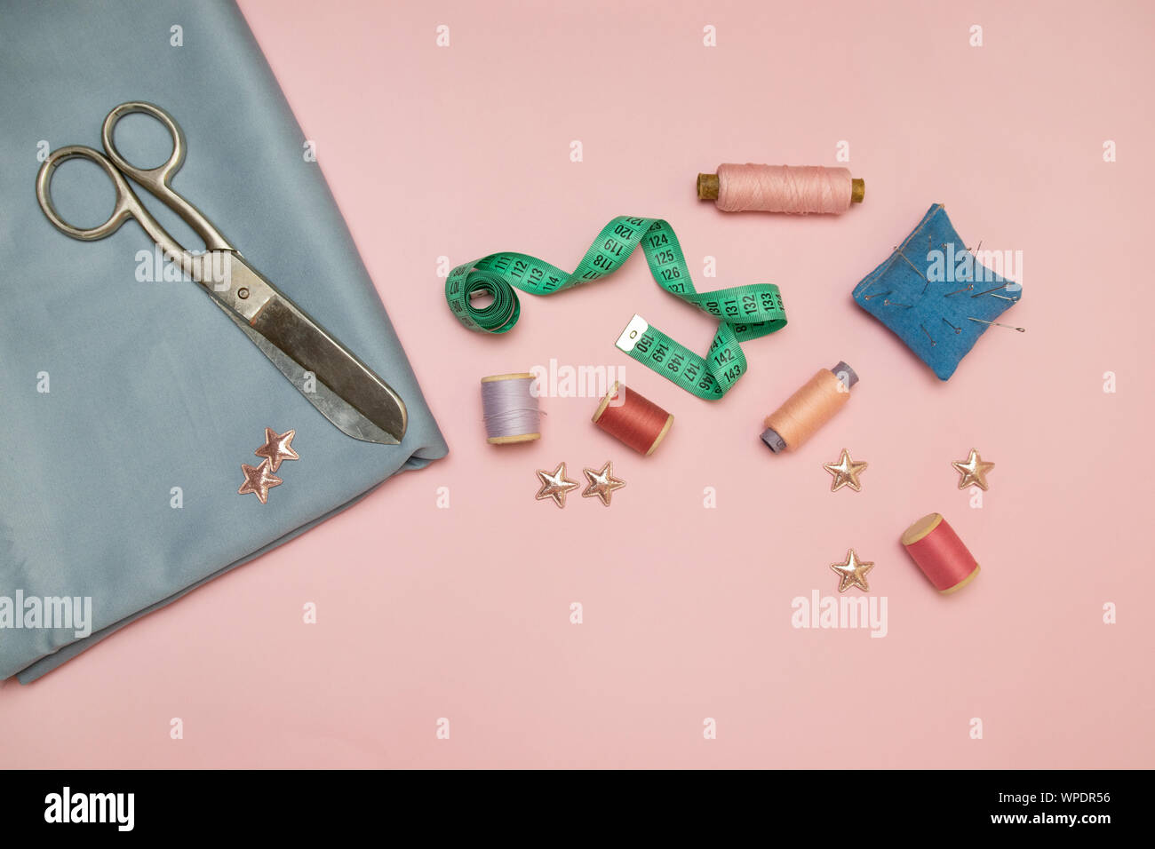 Outils de couture, tricot bleu pour la couture à l'aiguille, ciseaux et des bobines de fil de couleur sur un fond rose avec copie espace pour le texte Banque D'Images