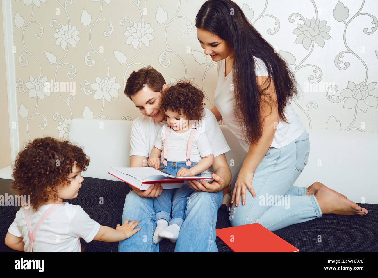 La mère et le père avec les enfants lire un livre tout en étant assis sur un canapé Banque D'Images