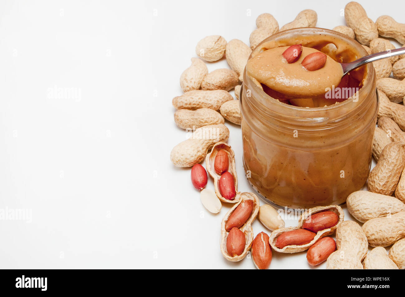 Le beurre d'arachide crémeux dans un bocal en verre, d'arachide et une cuillère isolé sur fond blanc. Un produit traditionnel de la cuisine américaine Banque D'Images
