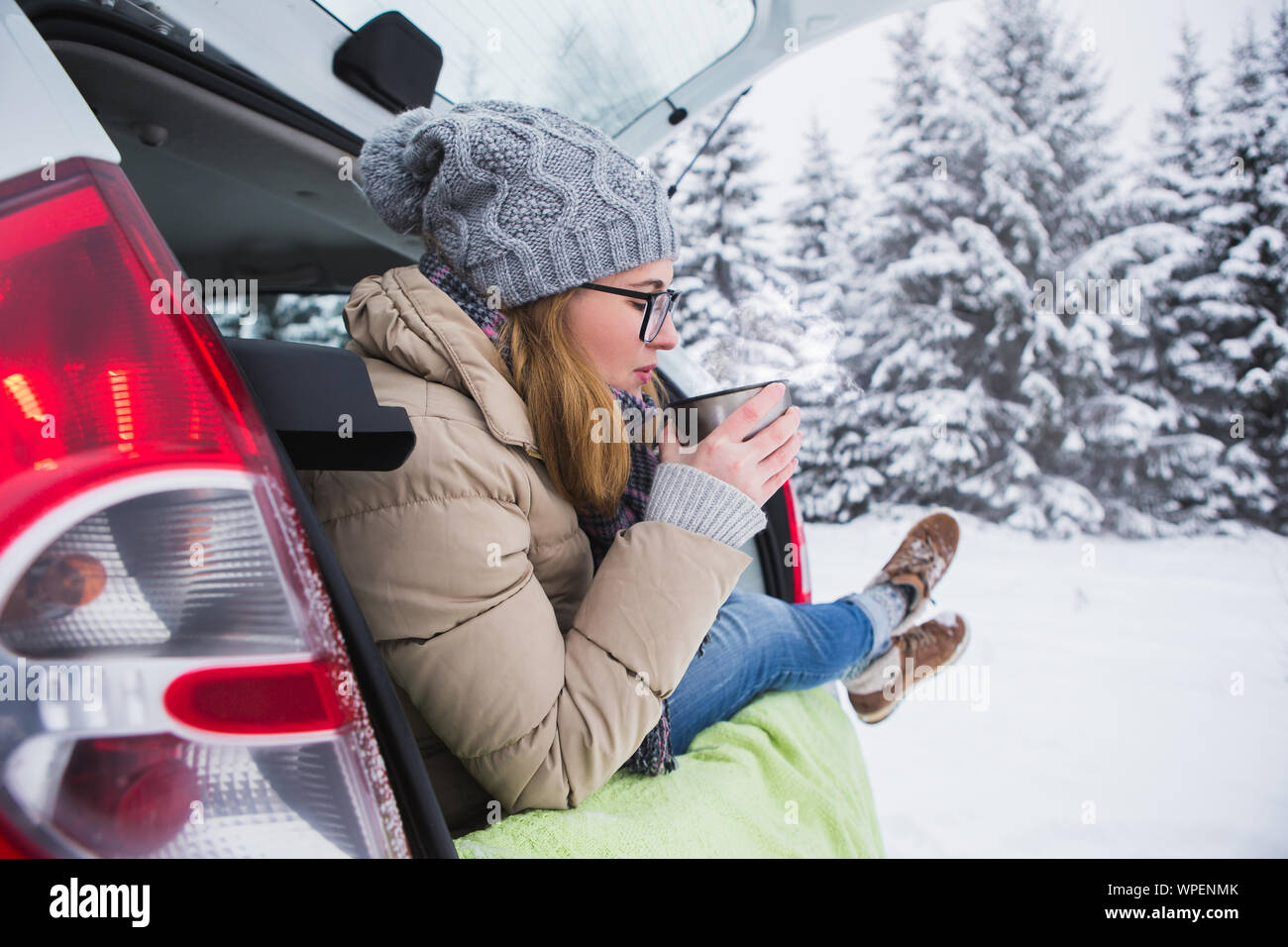 Young woman traveler se trouve dans le coffre de la voiture et est titulaire d'une tasse de thé dans les mains. Banque D'Images