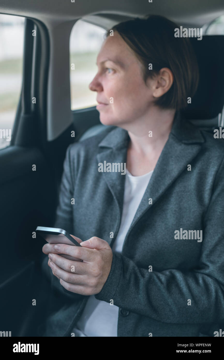 Businesswoman text messaging on mobile phone in car assis à la banquette arrière, selective focus Banque D'Images
