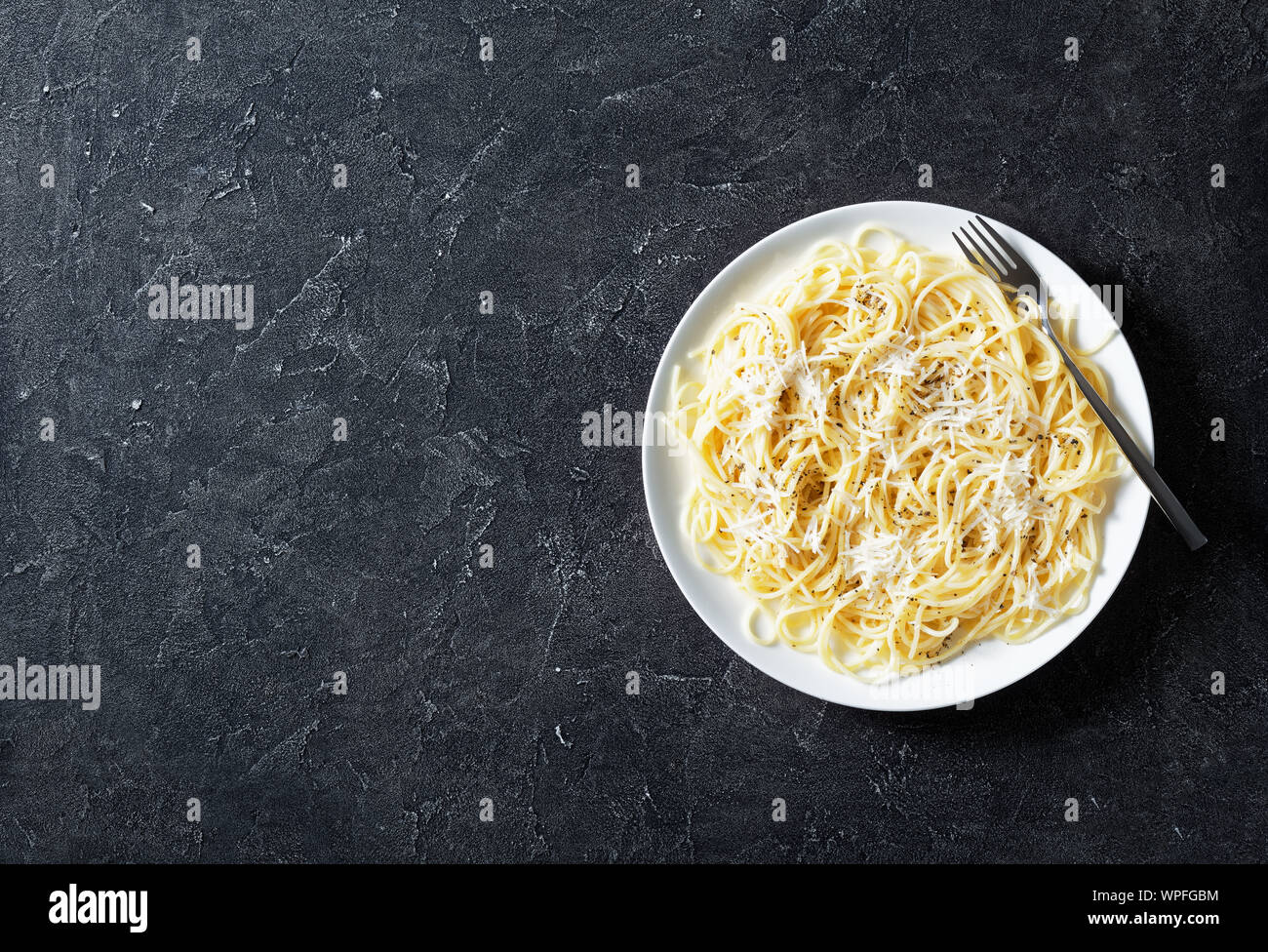 Belrom e pepe, spaghetti mélangée avec du fromage pecorino râpé et saupoudrées de poivre noir fraîchement moulu sur une plaque blanche avec une fourchette, vue de dessus, f Banque D'Images