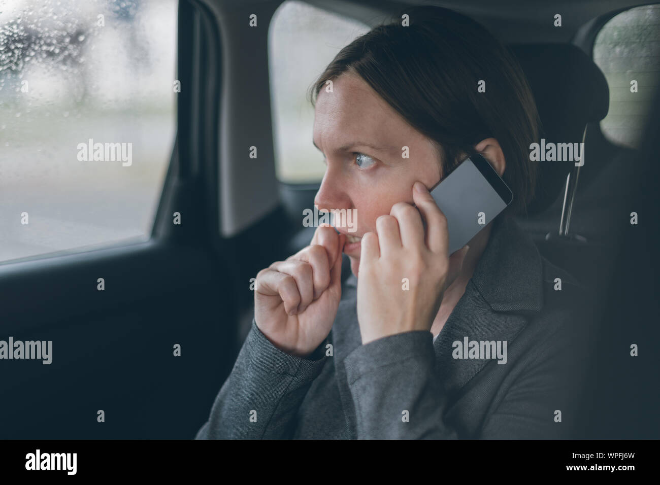 Femme d'ongles mordant nerveux et talking on mobile phone sur le siège arrière d'une voiture Banque D'Images