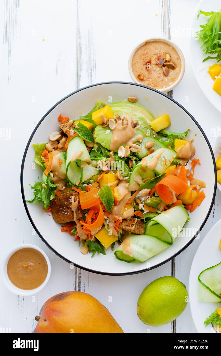 Salade fraîche d'été en bonne santé à la mangue, avocat, la chaux et le tofu avec vinaigrette sucrée du beurre d'arachide sur table en bois blanc Banque D'Images
