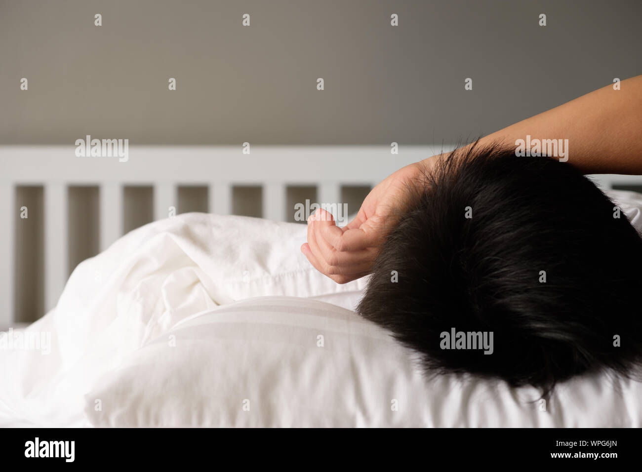 La femme est de mettre ses mains sur son front et est pensée sur le lit blanc. Banque D'Images