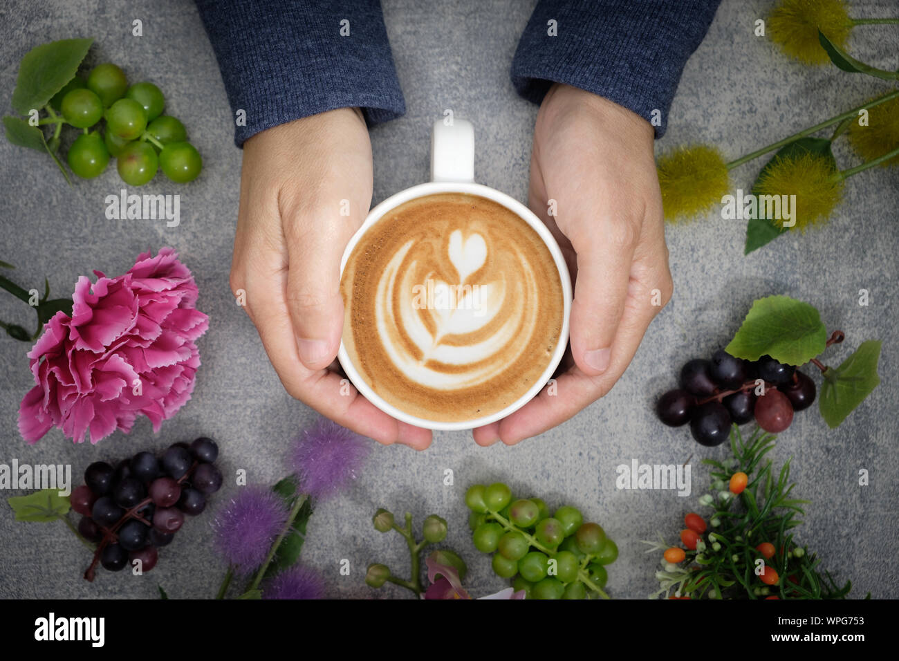 Les mains dans le chandail sont tenant une tasse de café et il y a beaucoup de fleurs colorées, entouré de raisin. Banque D'Images