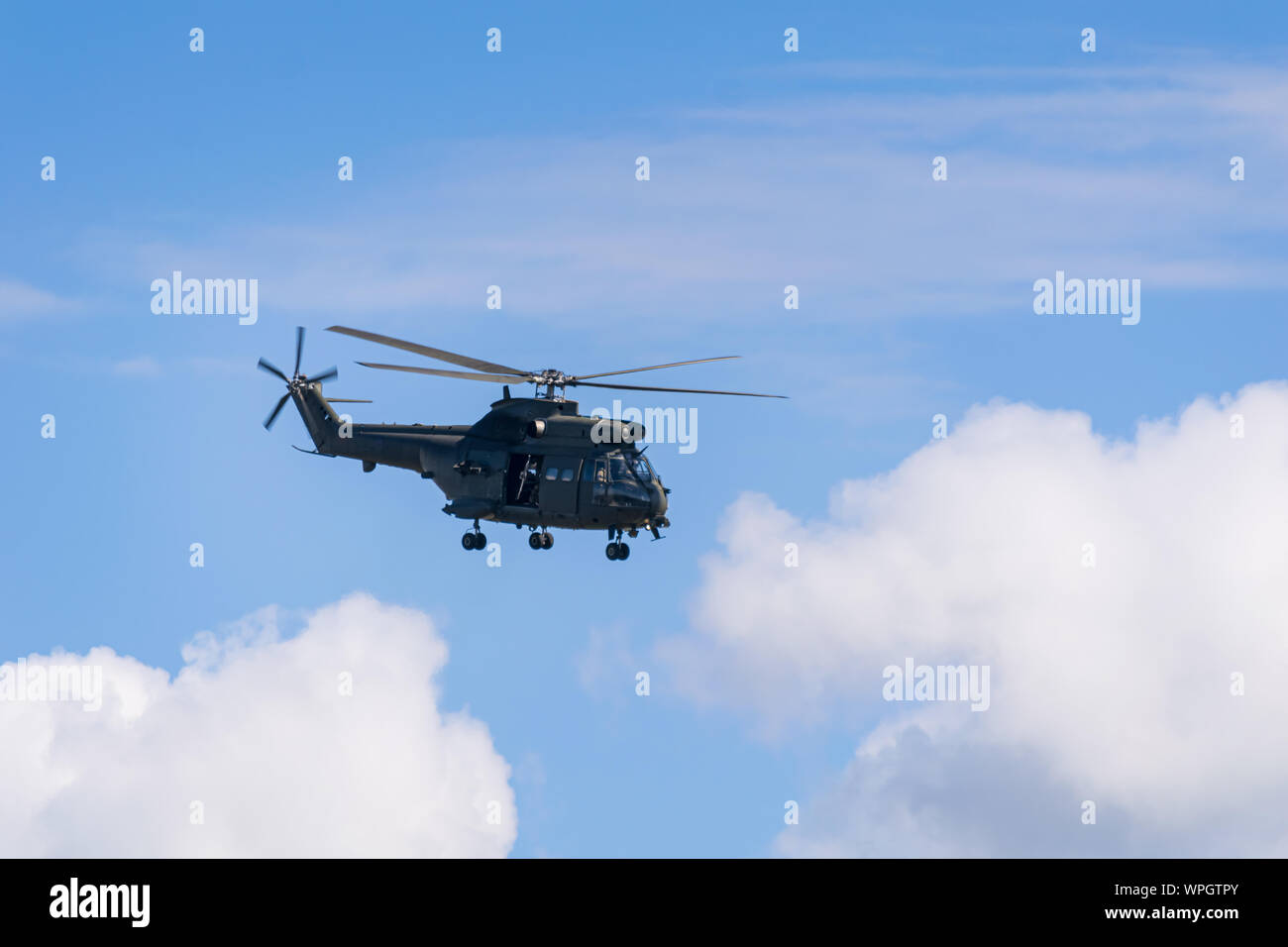 Un hélicoptère militaire plane dans les nuages sur une chaude journée d'été avec un ciel bleu Banque D'Images