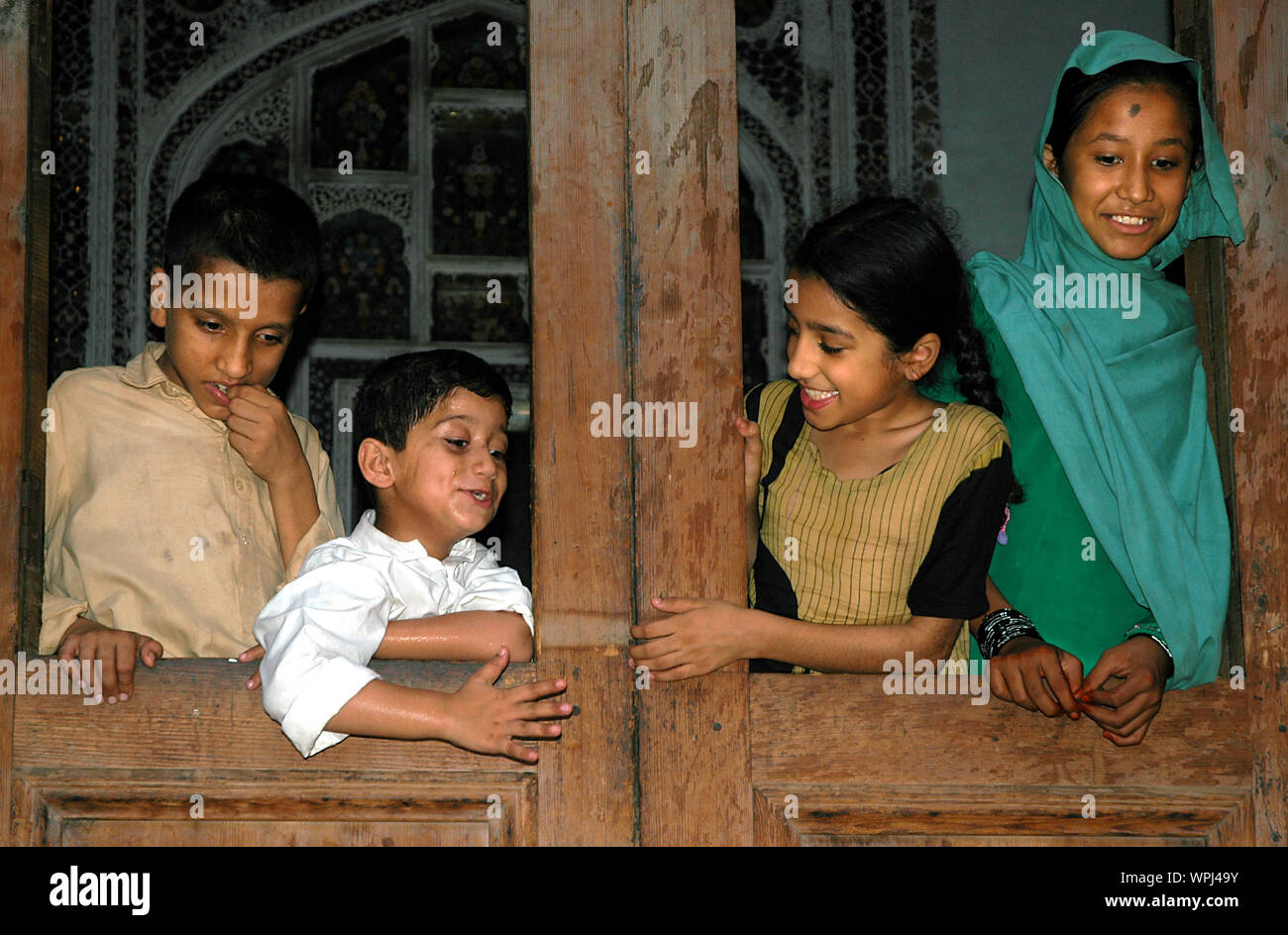 Quatre enfants regarder vers le bas à partir d'une fenêtre dans une maison à Peshawar, au Pakistan. 4 jeunes enfants pakistanais dans une vieille maison à Peshawar heureux et souriants. Banque D'Images