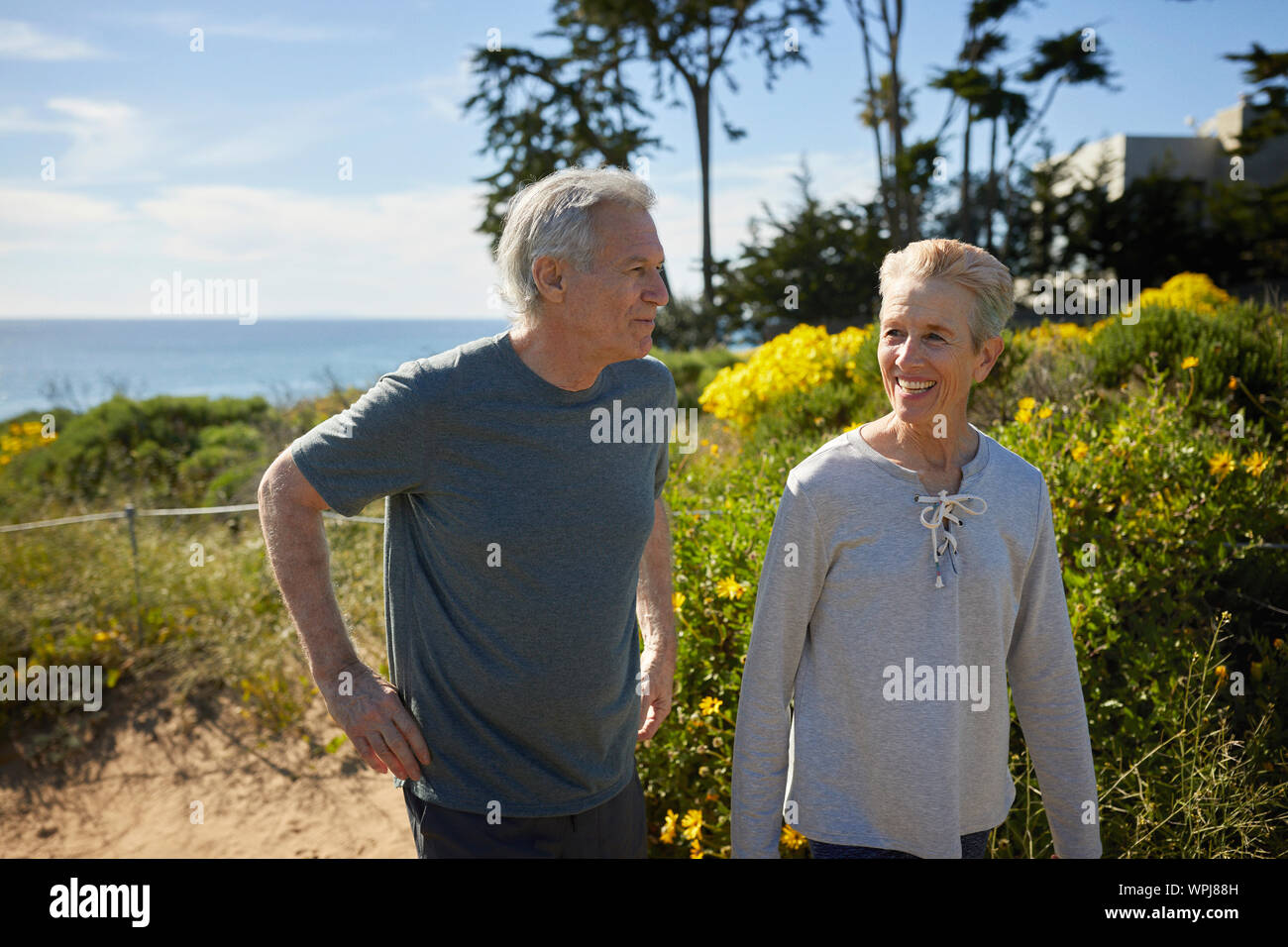 Happy senior couple talking tout en marchant par les plantes au cours de randonnées sur falaise against sky Banque D'Images