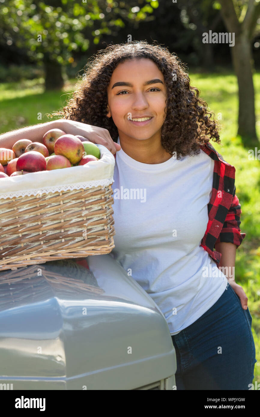 Belle happy mixed race African American girl biracial adolescent femme jeune femme souriante avec des dents parfaites dans un verger s'appuyant sur un tracteur wi Banque D'Images