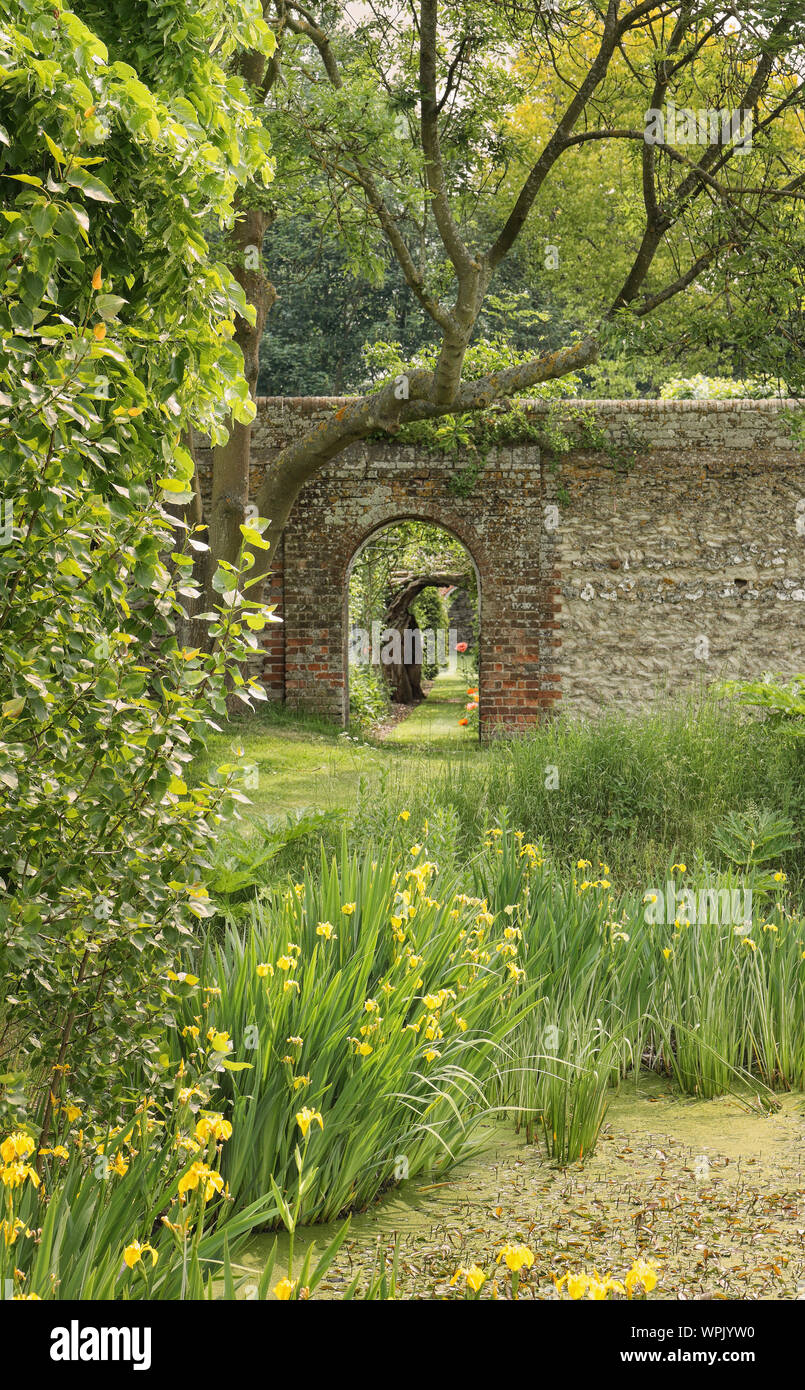 Passage voûté dans un anglais briques et silex avec jardin clos autour d'un étang, les iris Banque D'Images