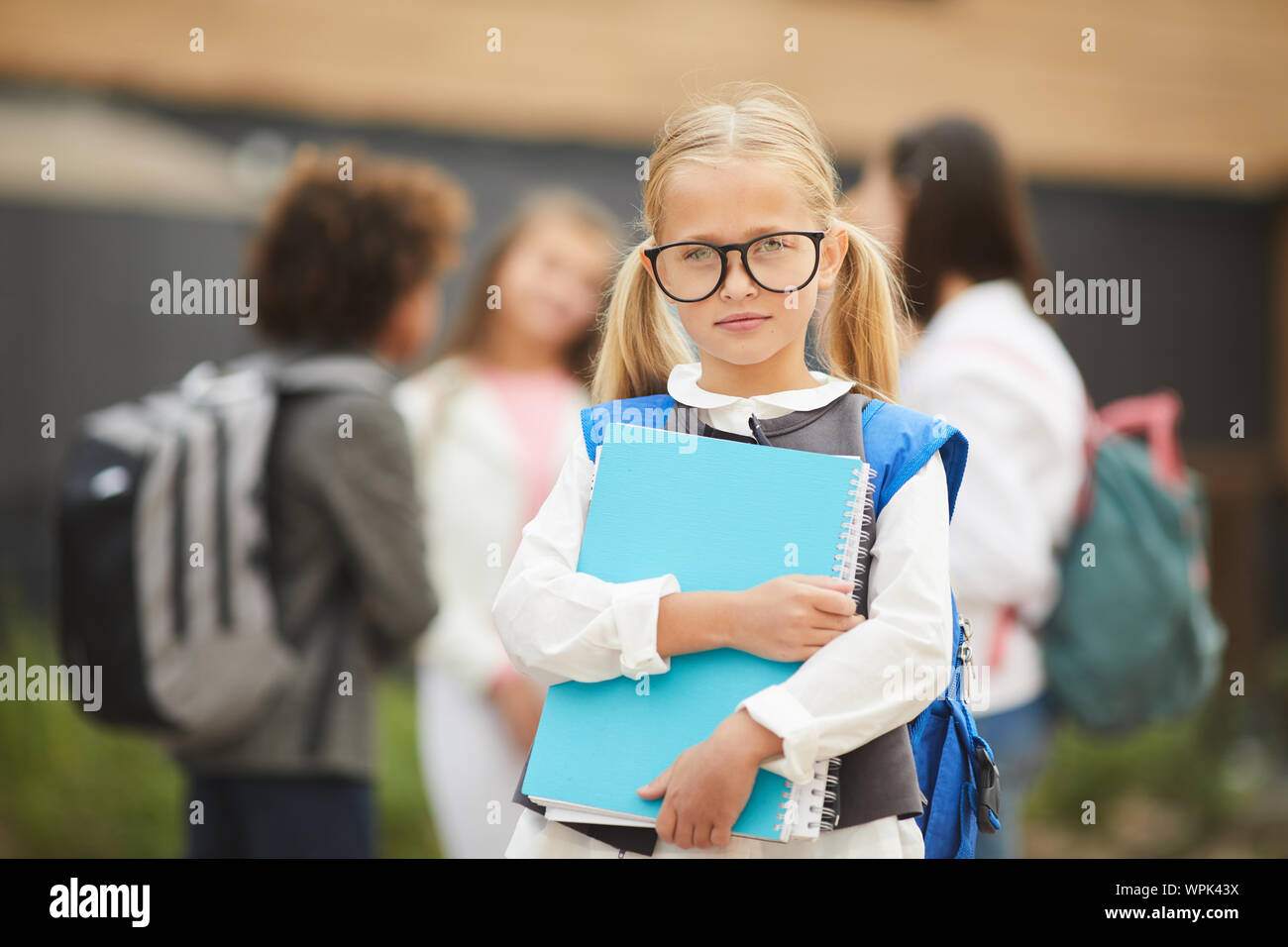 Portrait de lycéenne aux cheveux blonds dans les manuels scolaires et la tenue des lunettes à la caméra tout en se tenant à l'extérieur avec ses camarades dans la zone Banque D'Images