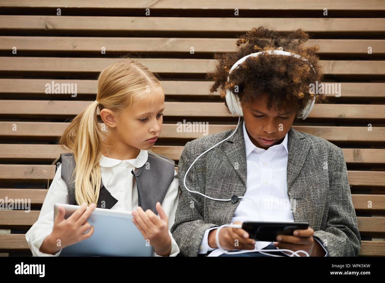 Écolier africain dans les écouteurs d'écouter de la musique sur son téléphone mobile avec l'aide d'écolière tablet pc ils assis sur le banc à l'extérieur Banque D'Images