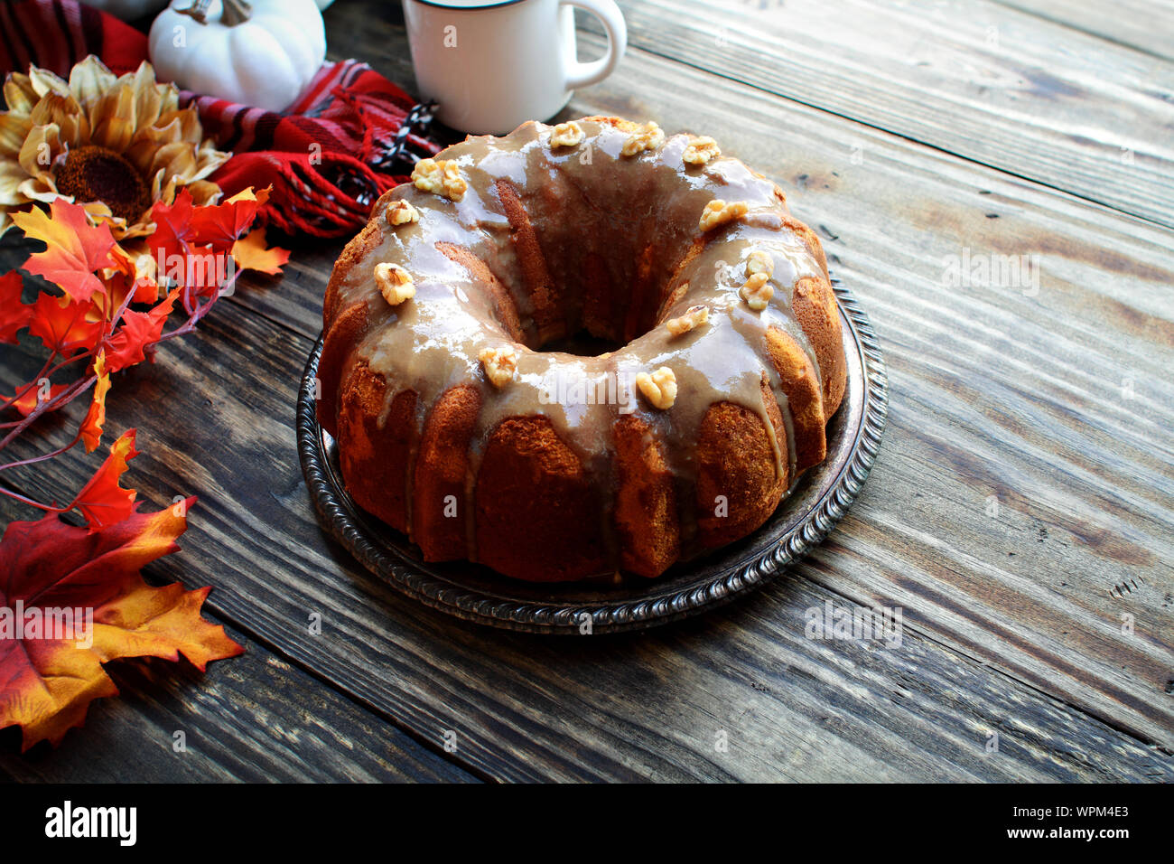 Citrouille, délicieux gâteau bundt épice givré avec glaçage de sucre brun et les noix avec les feuilles d'automne et de café sur une table en bois rustique, d'arrière-plan. Banque D'Images