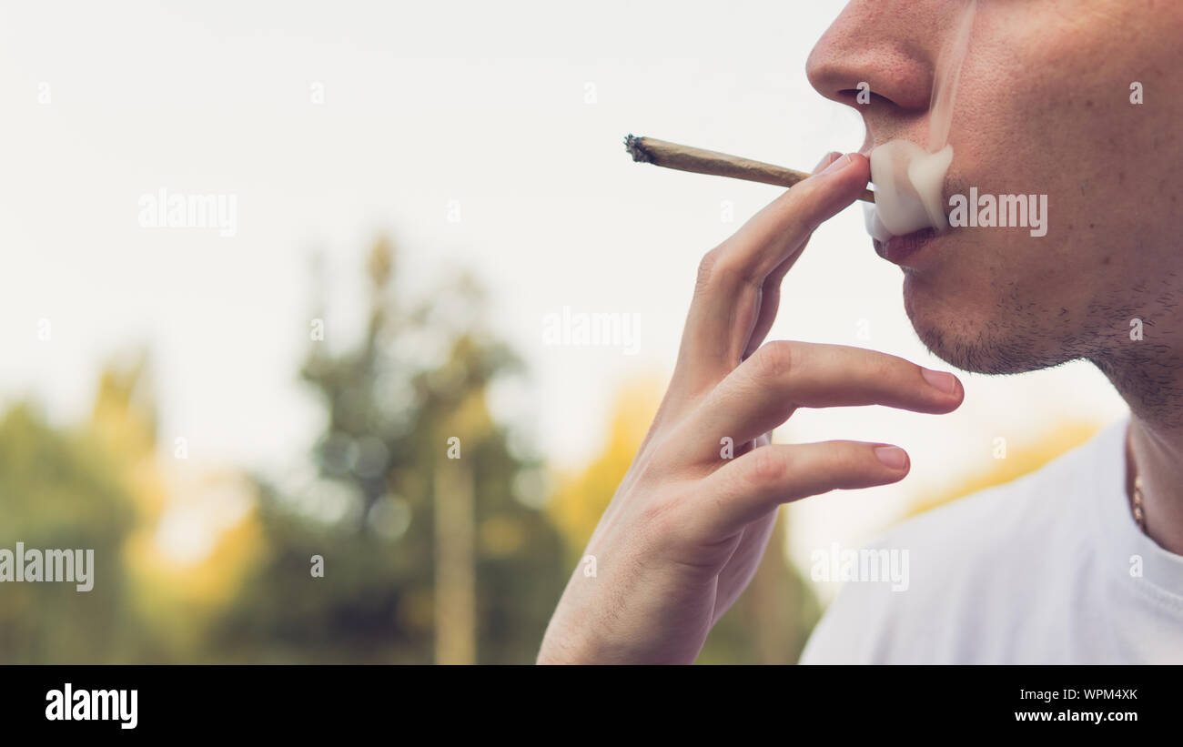 Le jeune fumeur de marijuana médicale à l'extérieur. conjointe Le jeune homme fumer du cannabis blunt, close-up. Le cannabis est un concept de médecine de fines herbes. Banque D'Images