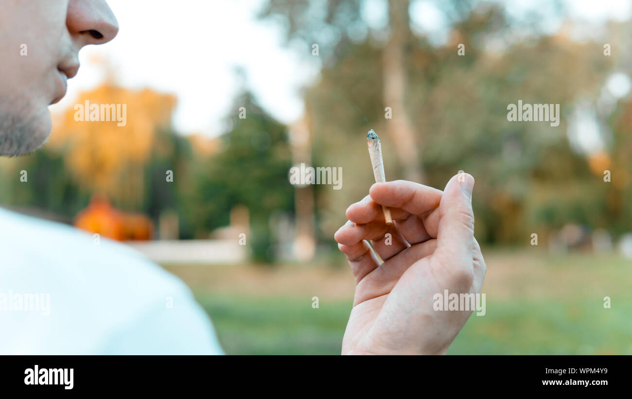 Le jeune fumeur de marijuana médicale à l'extérieur. conjointe Le jeune homme fumer du cannabis blunt, close-up. Le cannabis est un concept de médecine de fines herbes. Banque D'Images