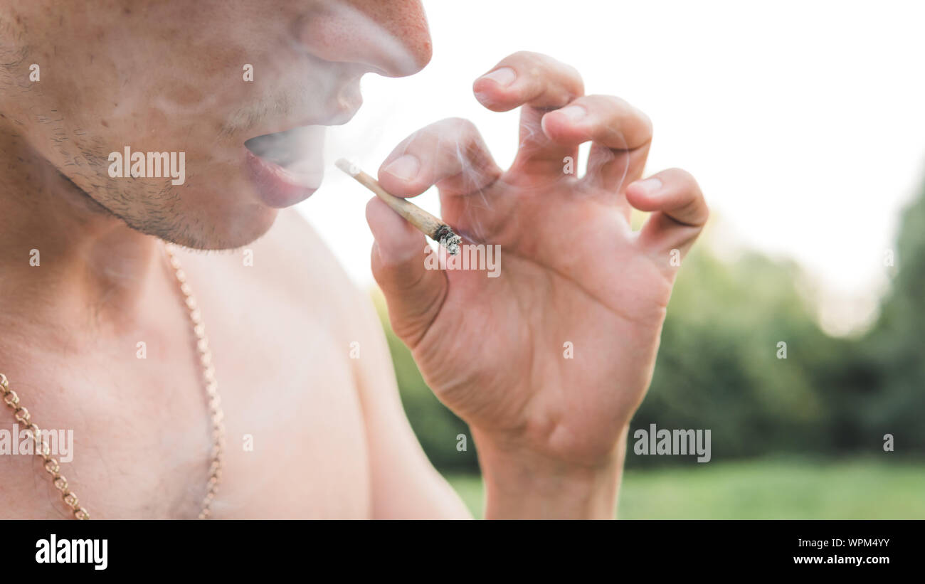 Le jeune fumeur de marijuana médicale à l'extérieur. conjointe Le jeune homme fumer du cannabis blunt, close-up. Le cannabis est un concept de médecine de fines herbes. Banque D'Images