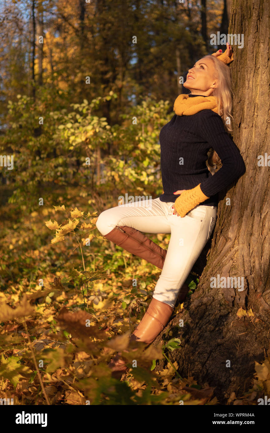 La fille repose sur un arbre et est photographiée au coucher du soleil dans des vêtements de cowboy, pieds de bottes bruns sur un arbre Banque D'Images