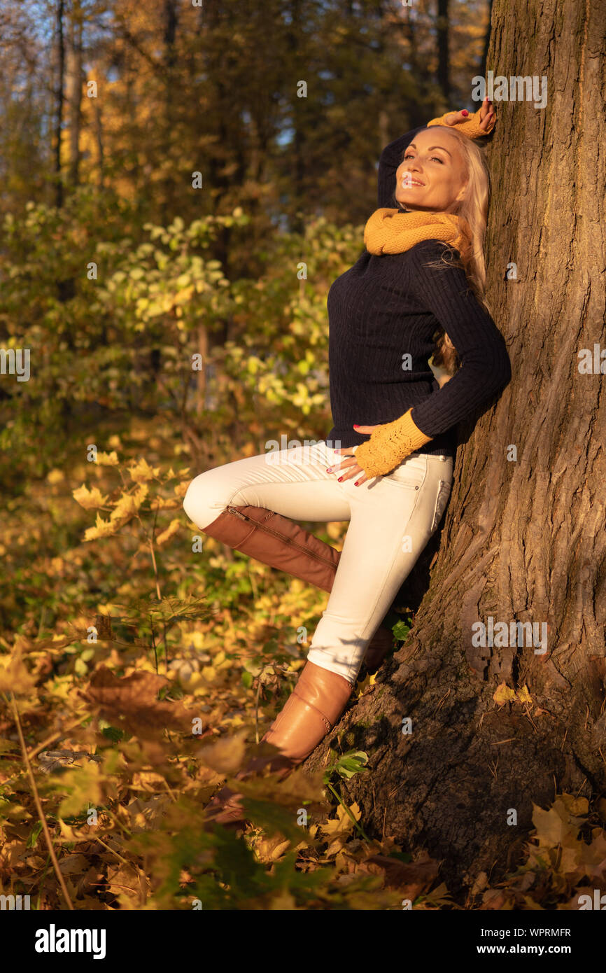 La fille repose sur un arbre et est photographiée au coucher du soleil dans des vêtements de cowboy, marron bottes jambe sur un arbre face à côté Banque D'Images