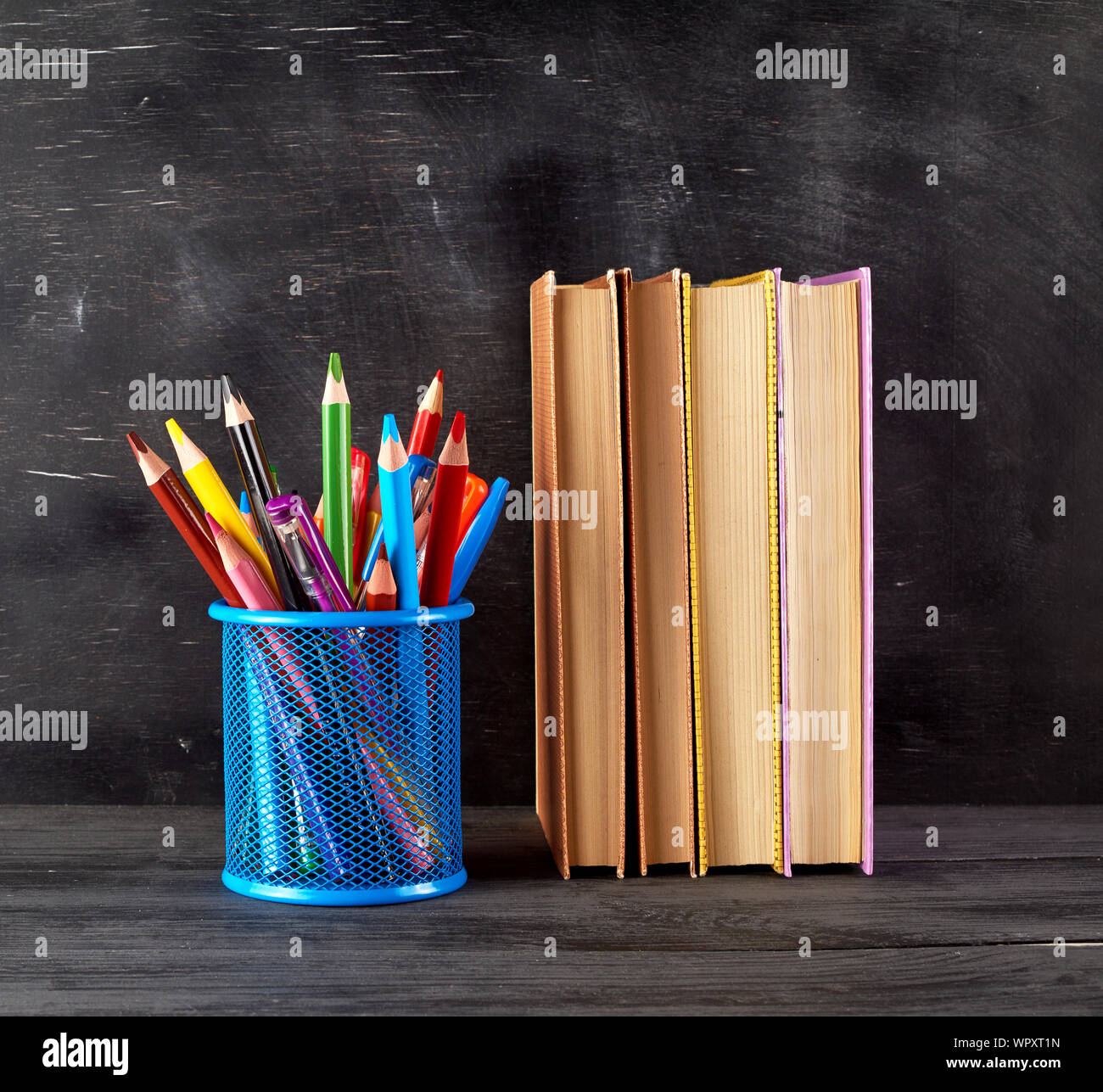 Pile de livres et d'une papeterie bleu verre avec multi-couleur crayons en bois, l'arrière-plan d'une craie noire vide, concept retour à l'école Banque D'Images