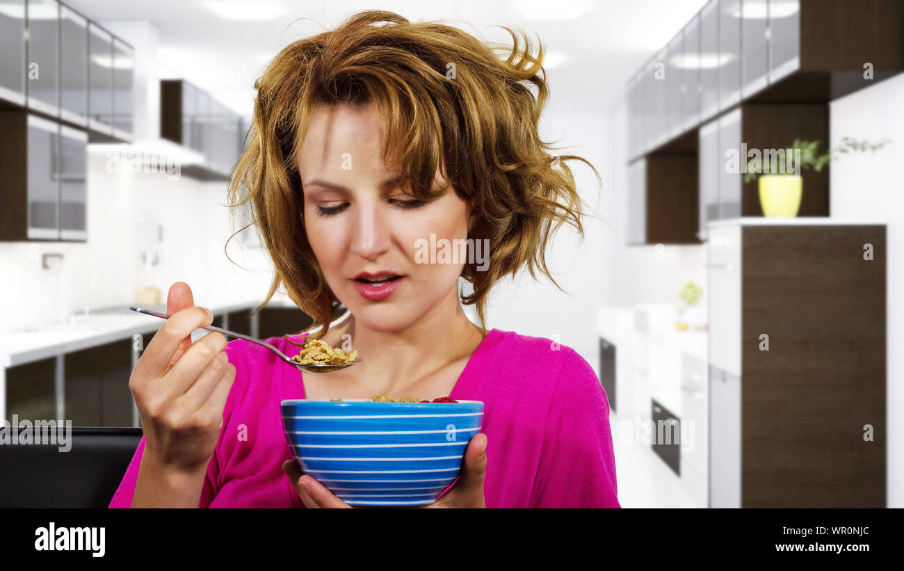 Les femmes de race blanche avec les cheveux crépus assise sur un sofa de manger un bol de céréales de petit-déjeuner. Elle est à la maison et regarde comme elle vient de se réveiller et de faire un mo Banque D'Images Les femmes de race blanche avec les cheveux crépus assise sur un sofa de manger un bol de céréales de petit-déjeuner. Elle est à la maison et regarde comme elle vient de se réveiller et de faire un mo Banque D'Images