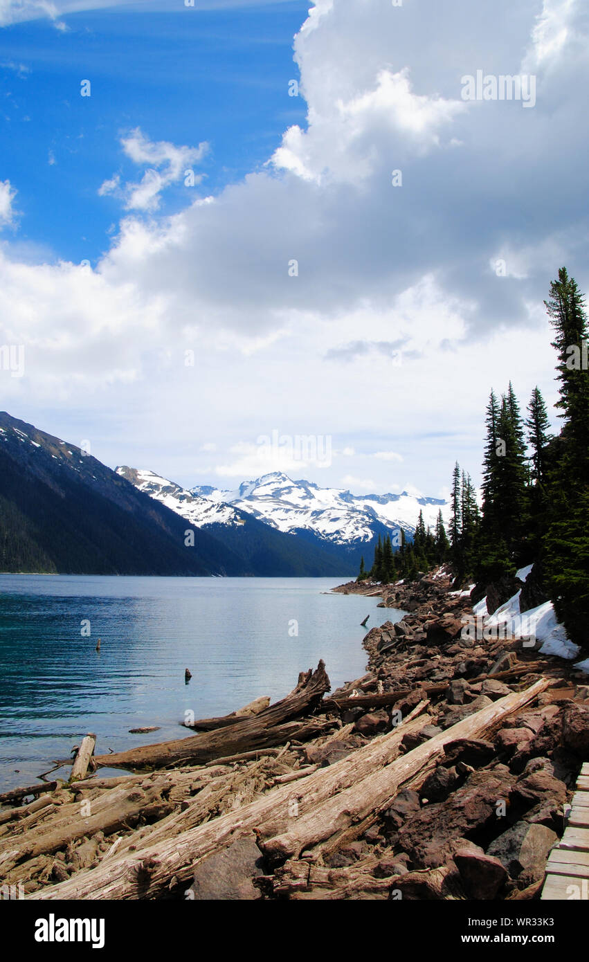 Turquoise et vert Garibaldi lake avec alpine et la forêt de conifères des montagnes enneigées à l'horizon, sur un sentier de randonnée dans le parc provincial Garibaldi Banque D'Images