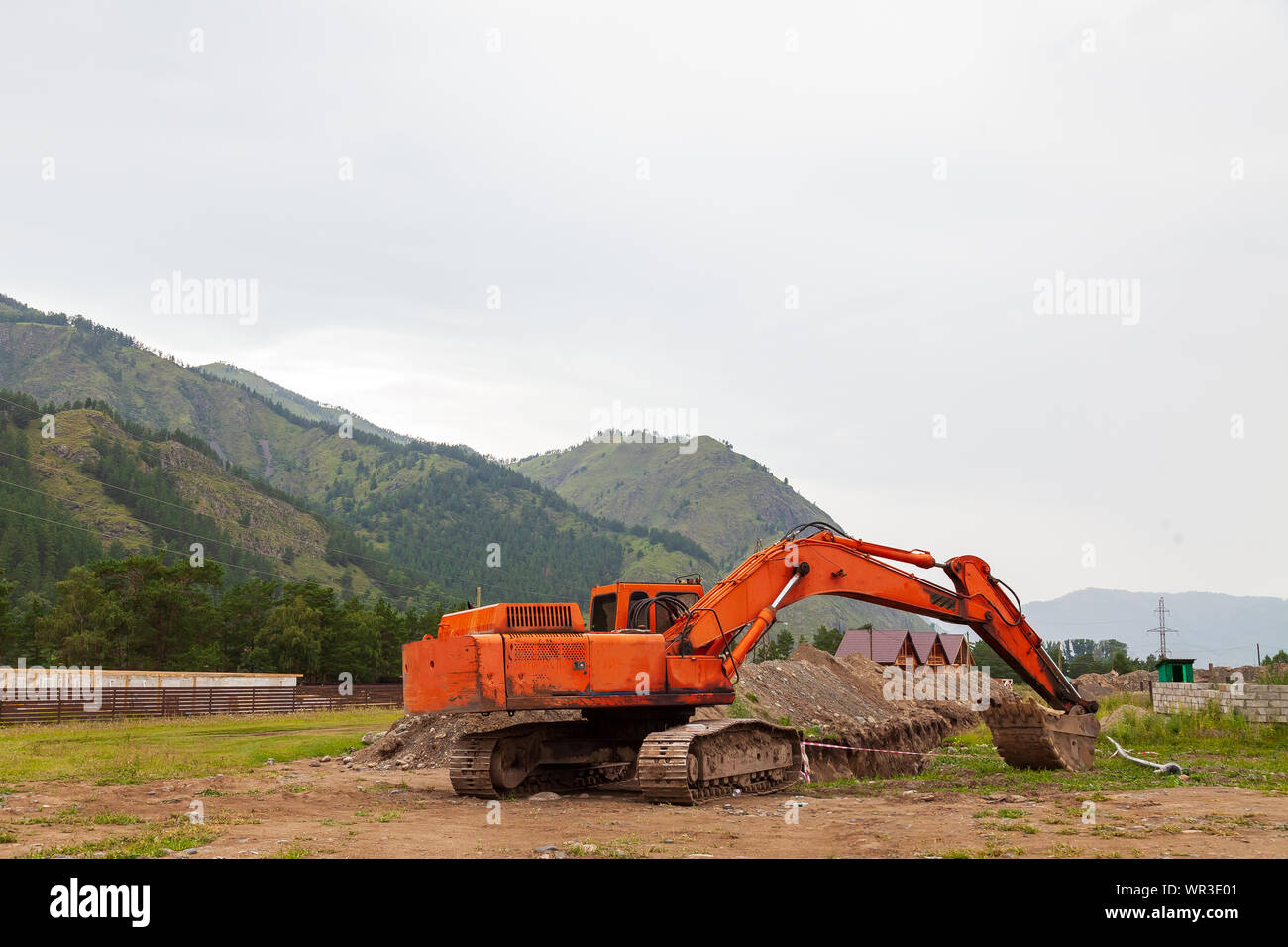 Grande pelle orange avec un godet abaissé durant les travaux de réparation dans les montagnes un jour d'été. Banque D'Images