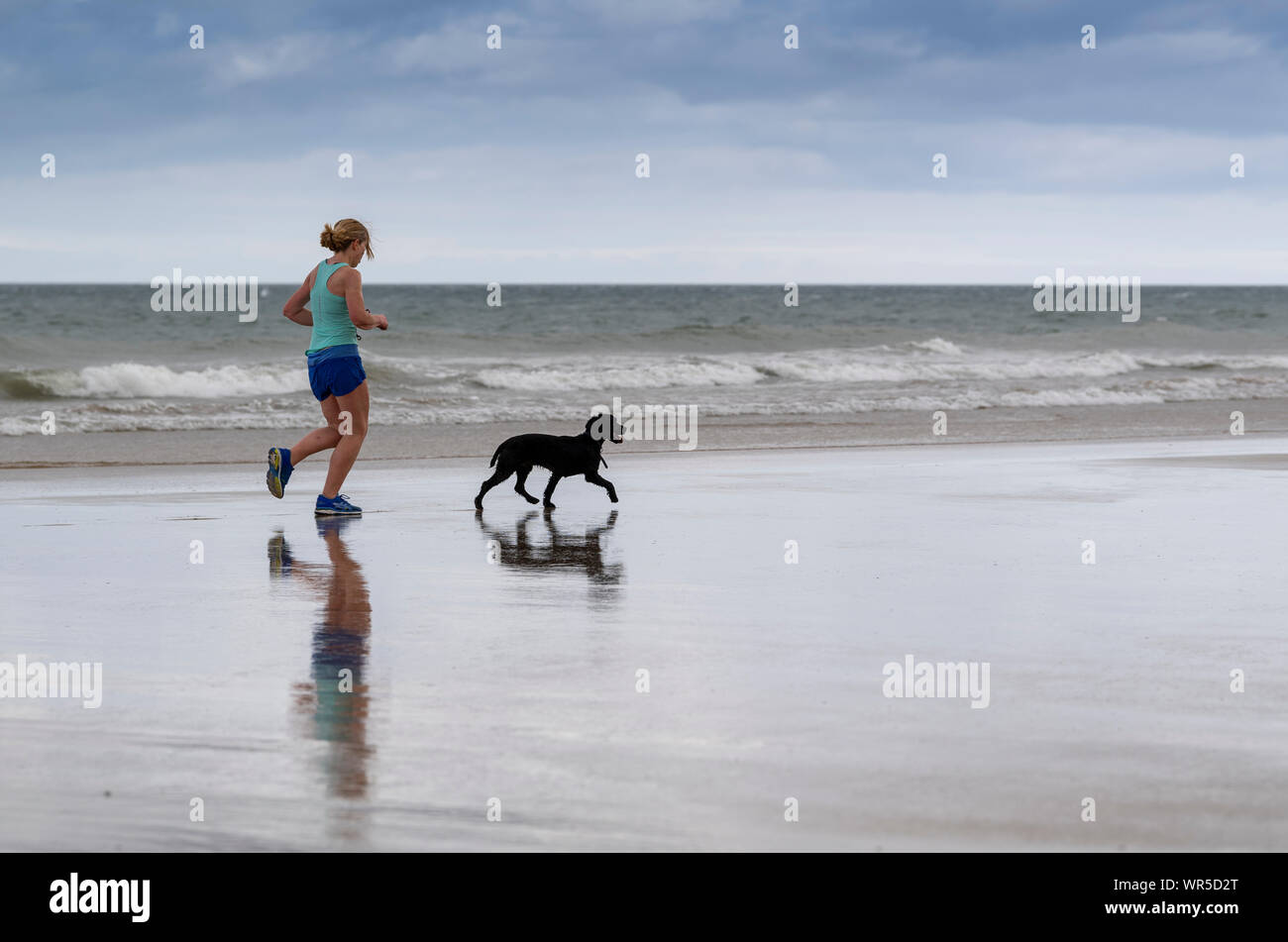 Woman jogging sur la plage de Benone avec son chien, l'Irlande du Nord, Royaume-Uni. Banque D'Images