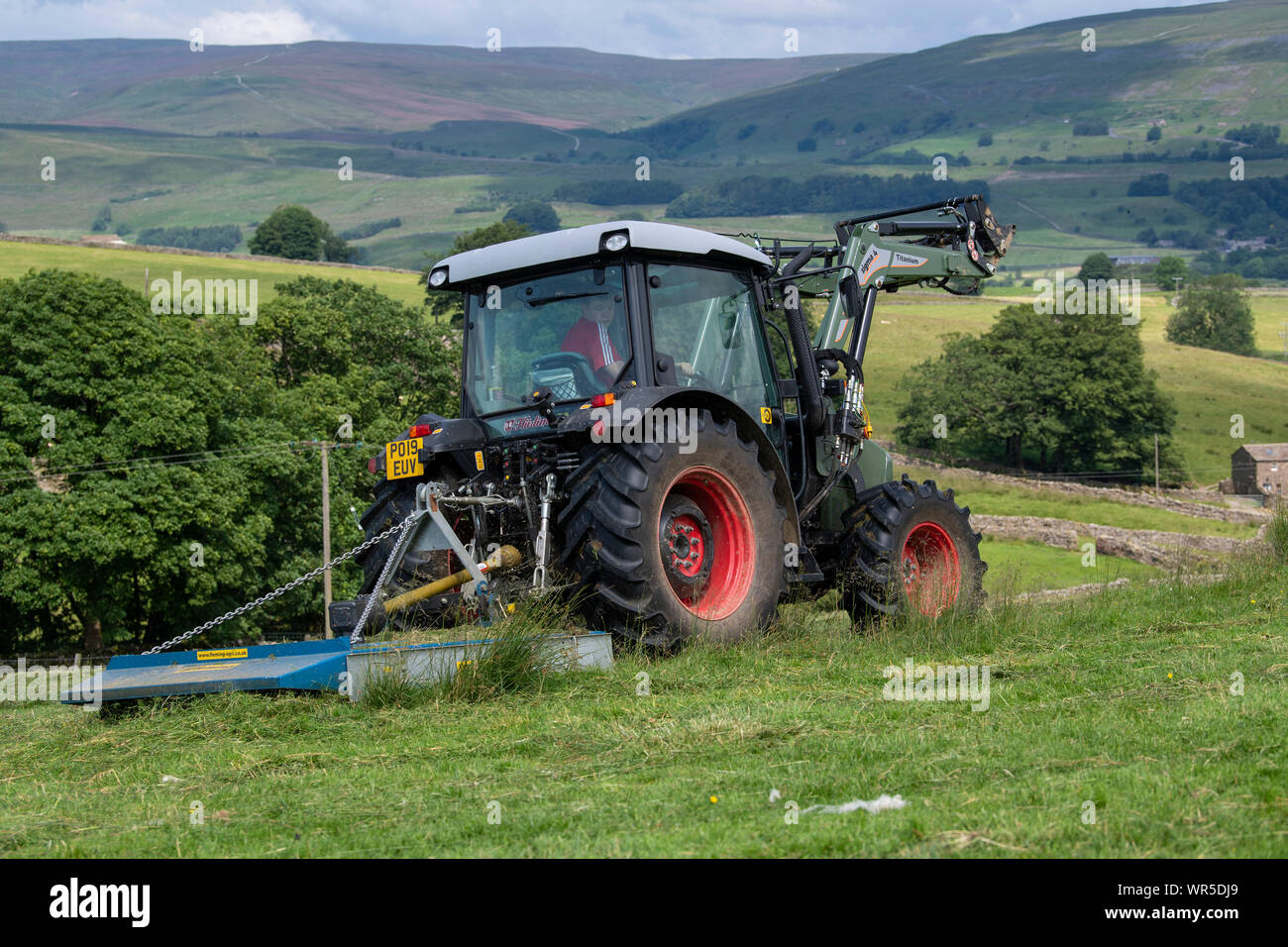 Envahi par l'herbe sur une garniture de pâturages de montagne avec un tracteur Hurlimann et un pâturage Fleming topper. North Yorkshire, UK. Banque D'Images