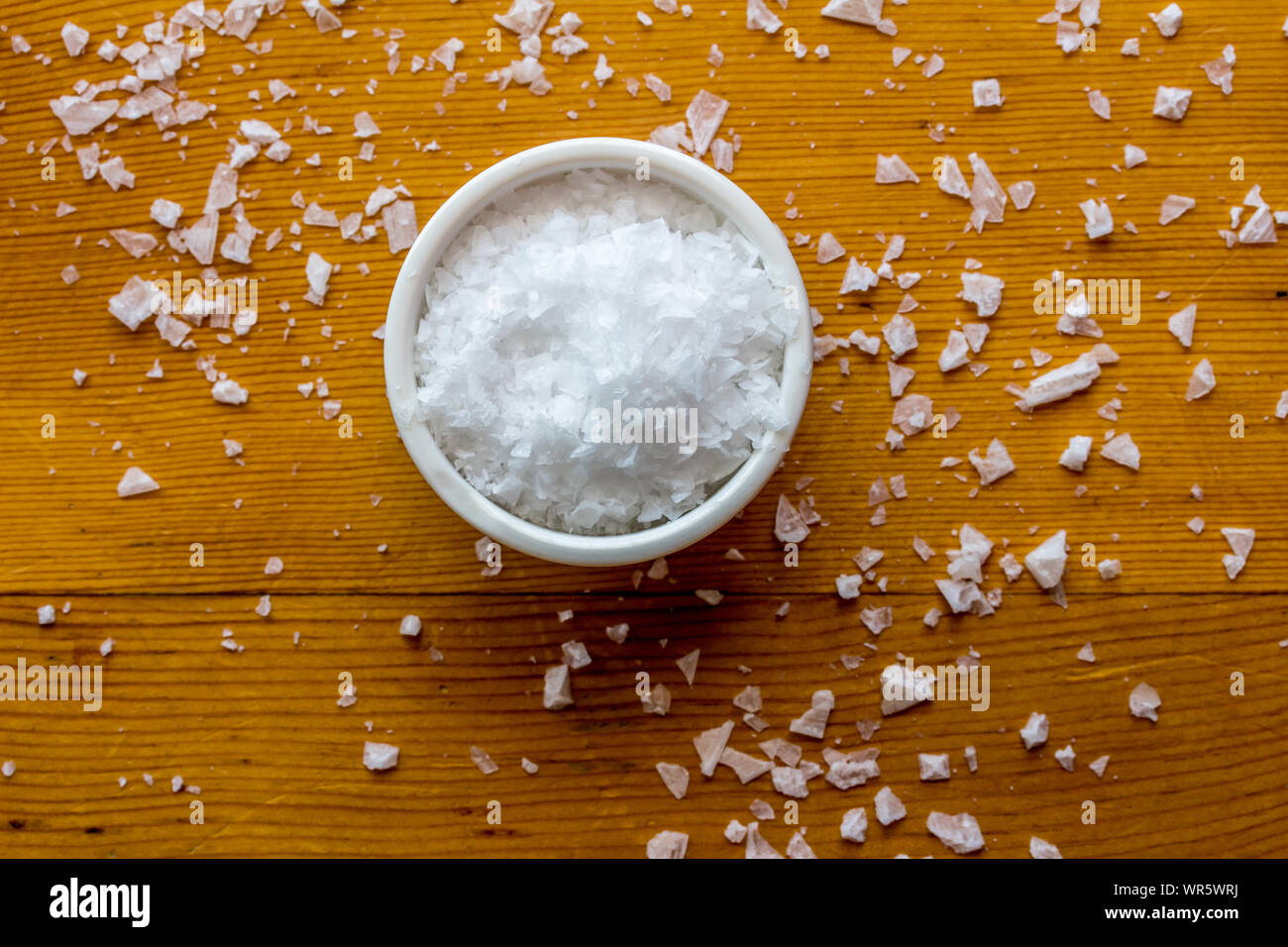Flocons de sel de mer chypriote dans peu de bol blanc sur fond de table grain de bois - au-dessus de la photo avec selective focus Banque D'Images