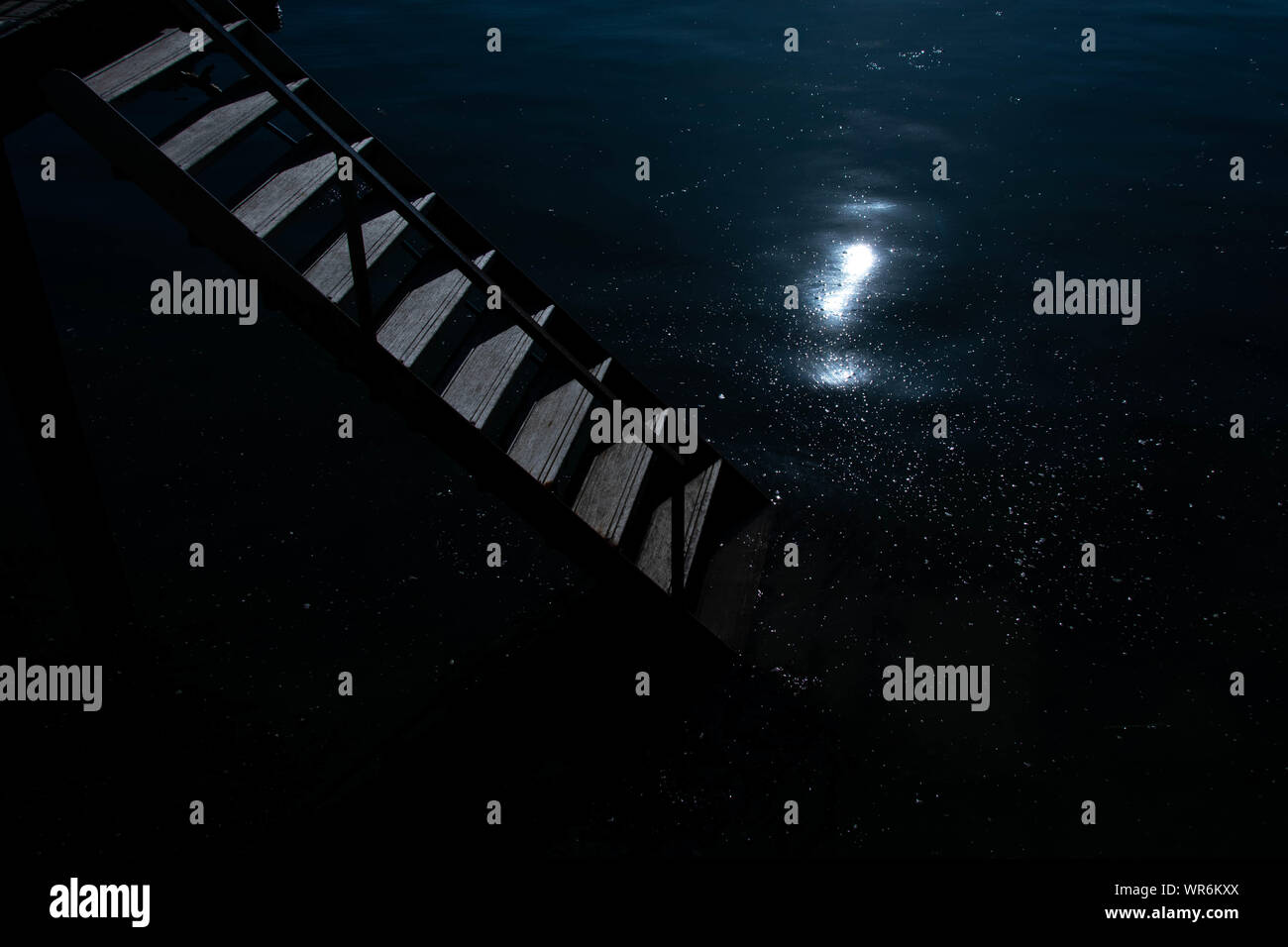 Un escalier descendant dans l'eau de nuit comme le clair de lune se reflète sur la surface des eaux Banque D'Images