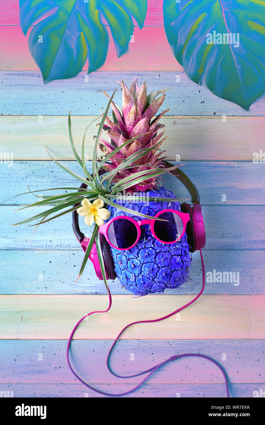 Ananas Hipster en violet lunettes de caractère et d'écouteurs à l'écoute de la musique. Les planches de bois rustique de lumière en arrière-plan, Vue de dessus, télévision lay Banque D'Images