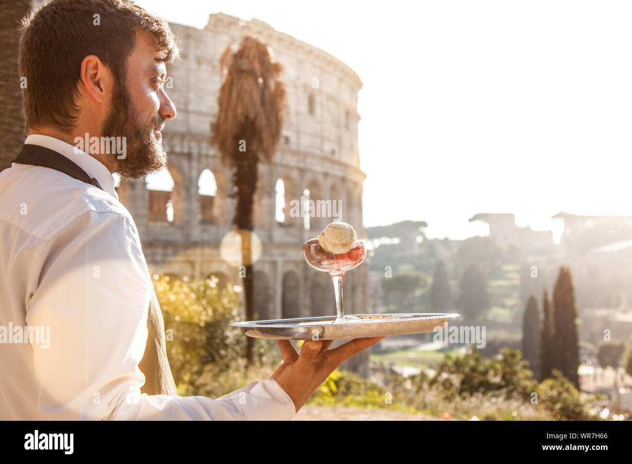 Waiter holding élégant servant un essayer avec un verre de glace colorée en face du Colisée à Rome au coucher du soleil Banque D'Images