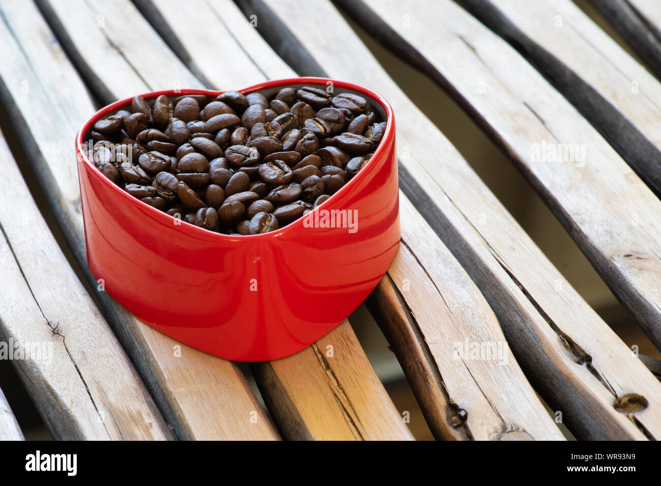 Grains de café dans une boîte en forme de coeur disposés sur un fond de bois. Banque D'Images