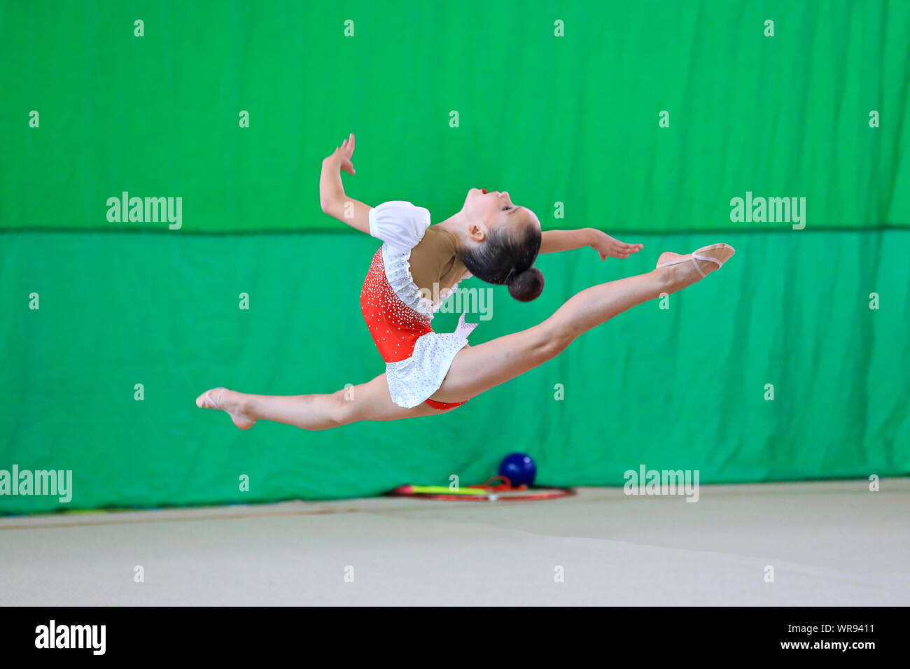 Moscou / Russie - 09/08/2019 : Jeune fille gymnaste exécute element Split bond en avant avec les jambes étendues. Gymnaste dans une robe blanche et rouge Banque D'Images