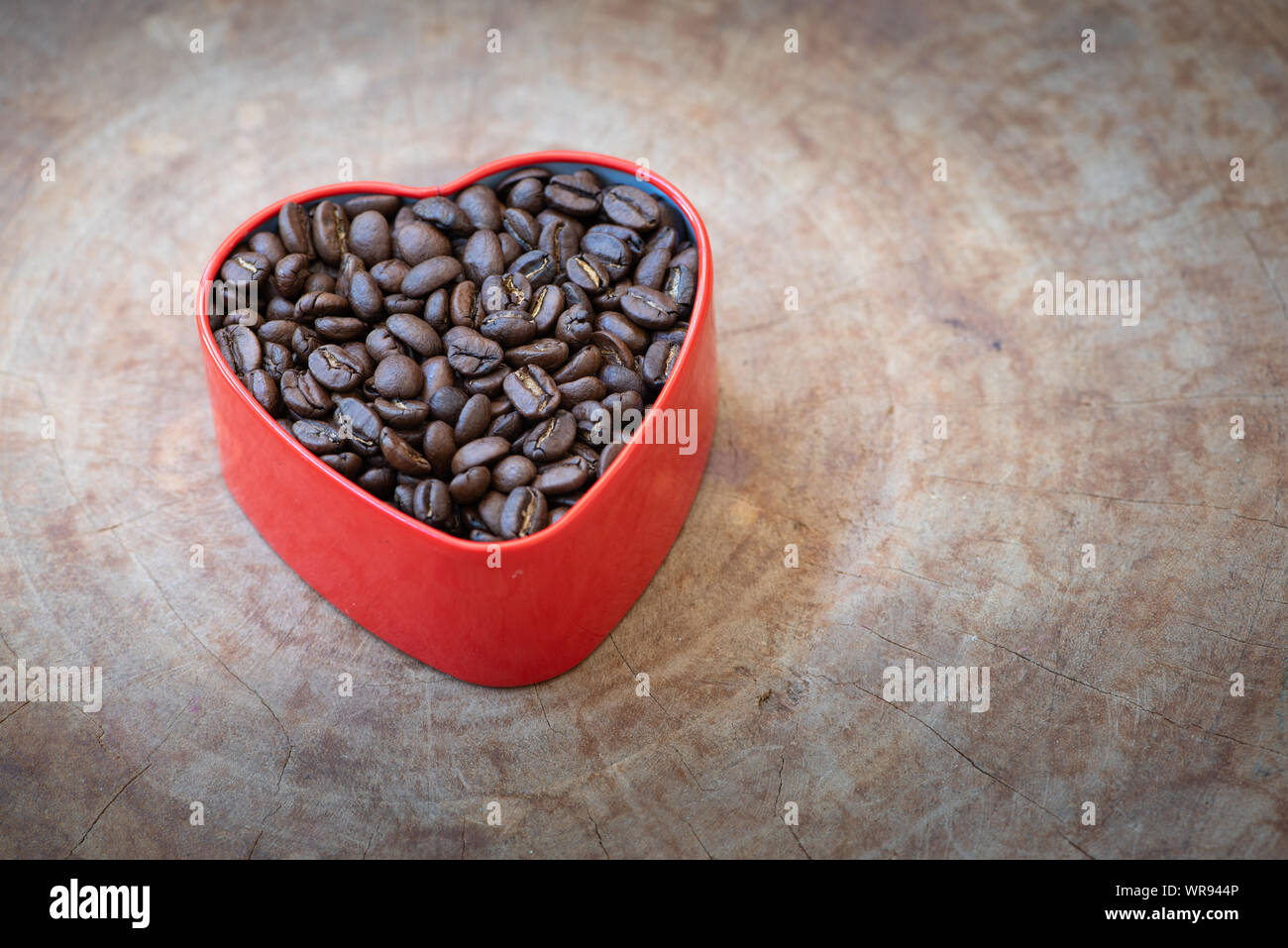 Grains de café dans une boîte en forme de coeur disposés sur un fond de bois. Banque D'Images