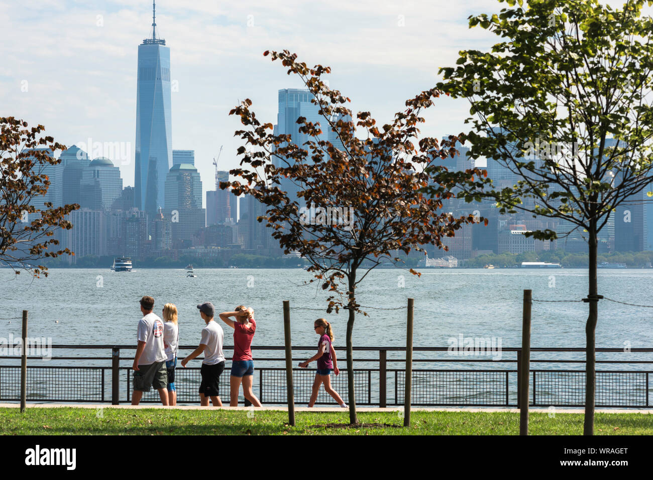 Famille New York, vue d'un groupe familial marchant sur Liberty Island avec les gratte-ciel de Lower Manhattan au loin, New York City, États-Unis. Banque D'Images