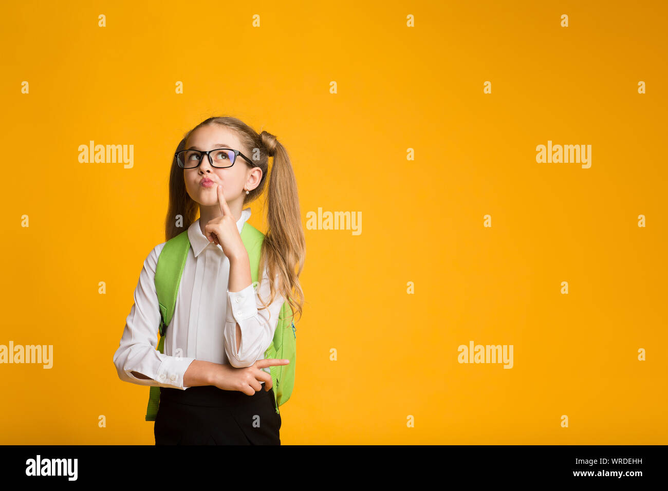 Élève d'école élémentaire Girl Thinking posant sur fond jaune. Banque D'Images