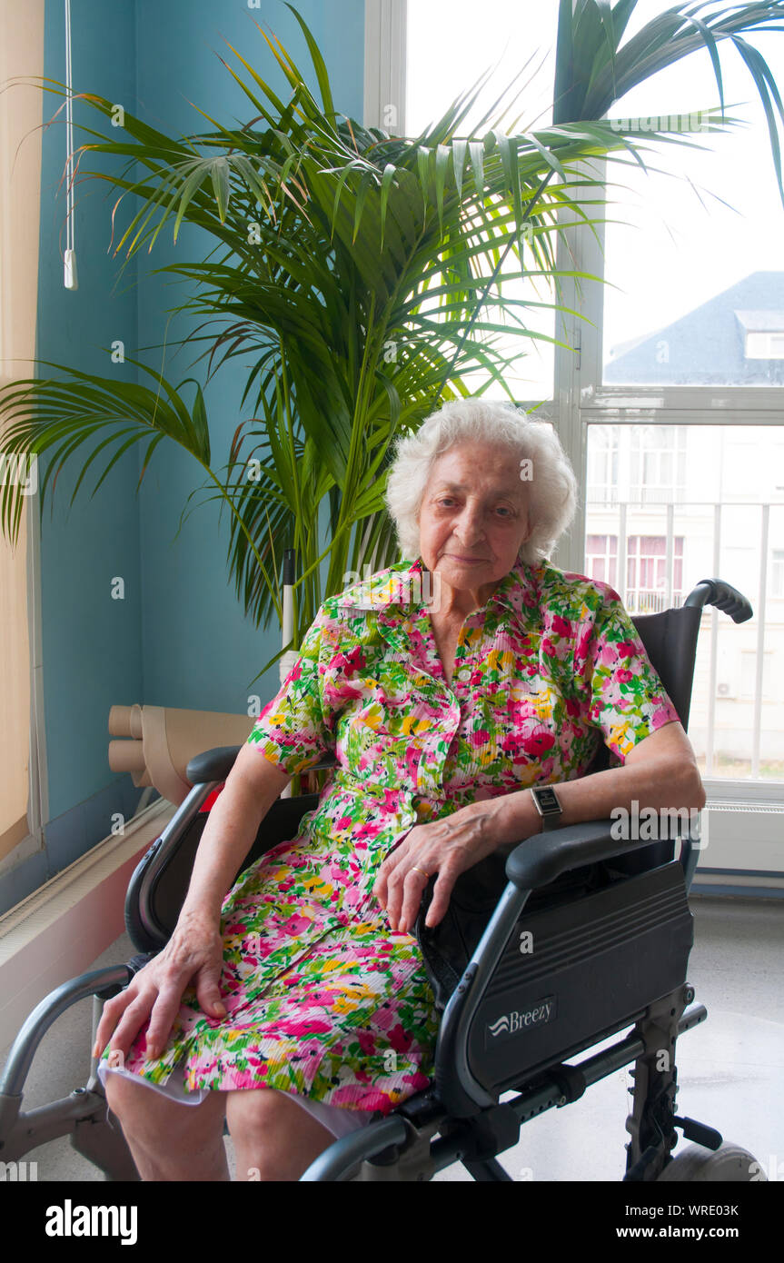 Vieille dame assise dans un fauteuil roulant, souriant et regardant la caméra. Banque D'Images