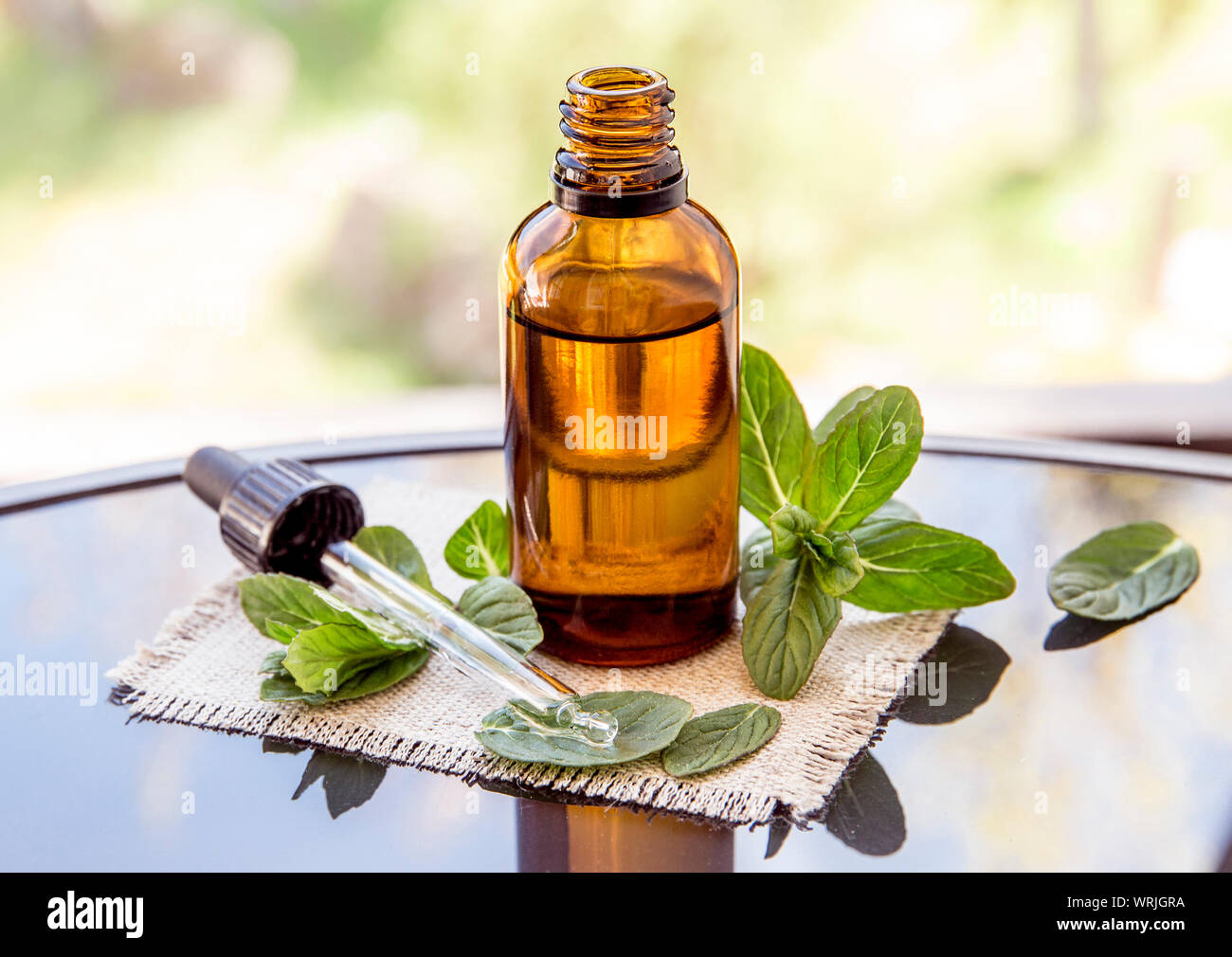 L'huile essentielle de menthe poivrée ou de l'infusion en bouteille pipette médicale brun avec des branches de menthe fraîche sur une table en verre, l'arrière-plan flou. Banque D'Images