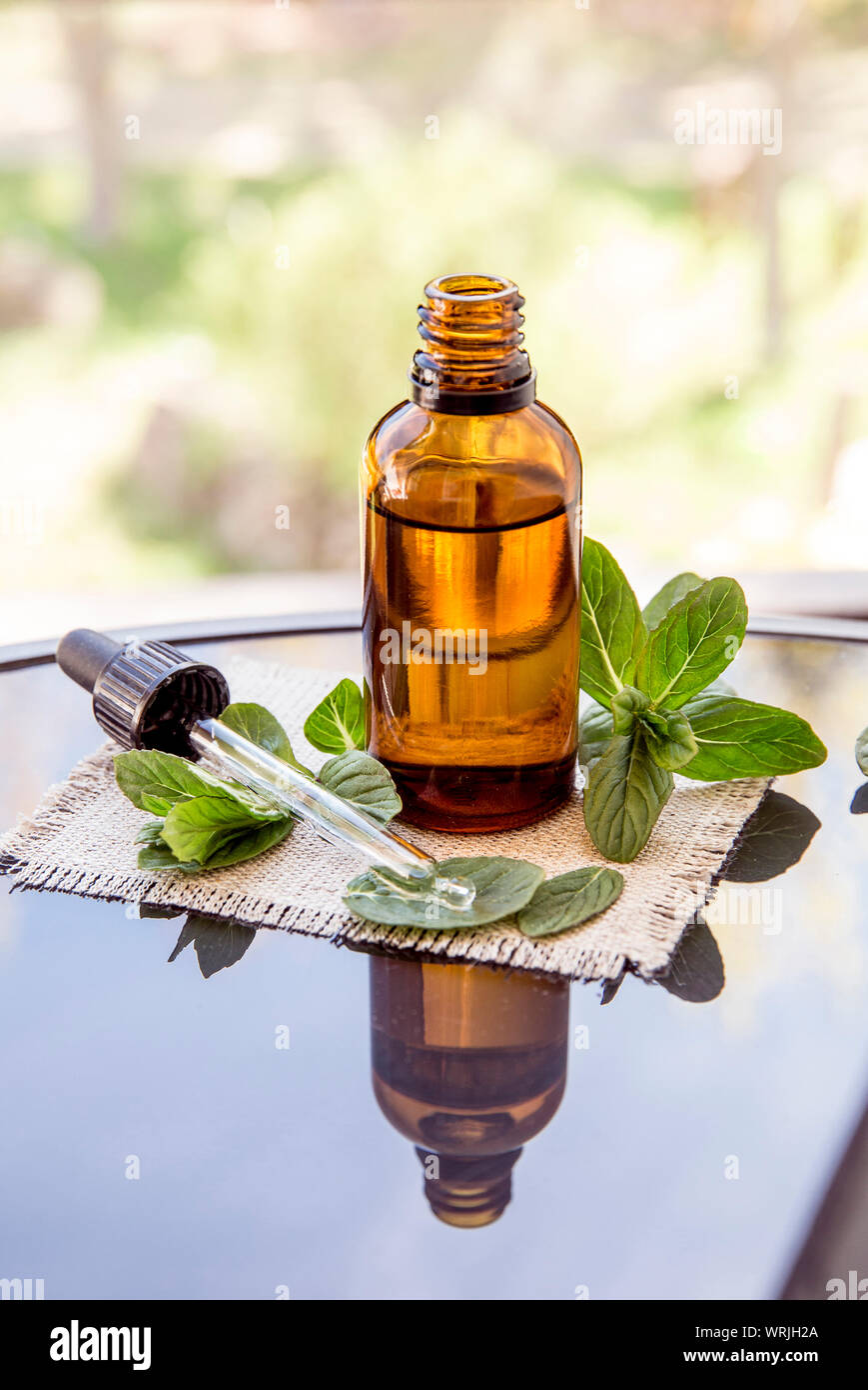 L'huile essentielle de menthe poivrée ou de l'infusion en bouteille pipette médicale brun avec des branches de menthe fraîche sur une table en verre, l'arrière-plan flou. Banque D'Images