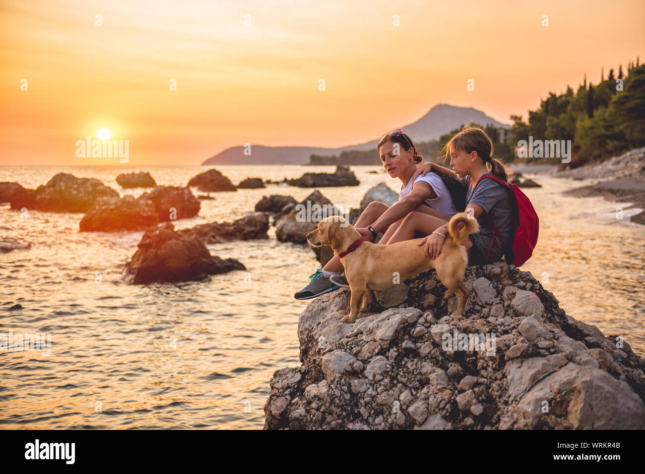 Mère et fille avec un petit chien jaune de la randonnée le long de la plage pendant le coucher du soleil Banque D'Images Mère et fille avec un petit chien jaune de la randonnée le long de la plage pendant le coucher du soleil Banque D'Images