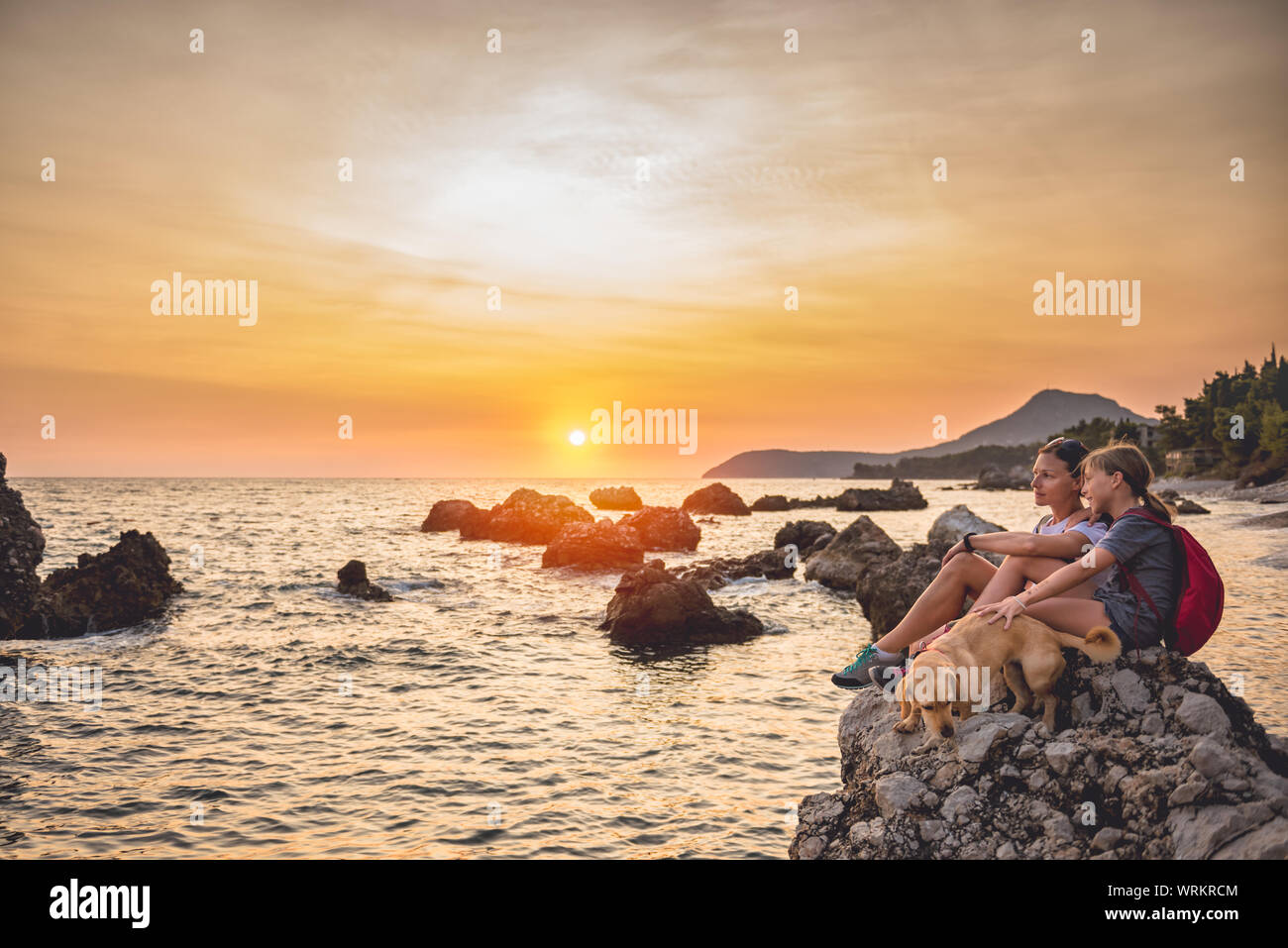 Mère et fille avec un petit chien jaune de la randonnée le long de la plage pendant le coucher du soleil Banque D'Images Mère et fille avec un petit chien jaune de la randonnée le long de la plage pendant le coucher du soleil Banque D'Images